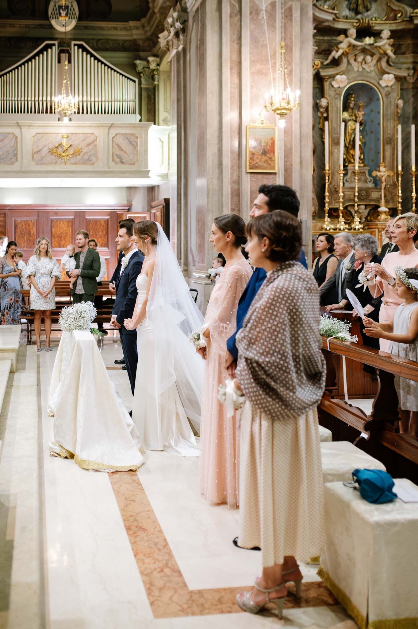 Elegant church interior during wedding ceremony with guests standing in pews and ornate pipe organ visible.