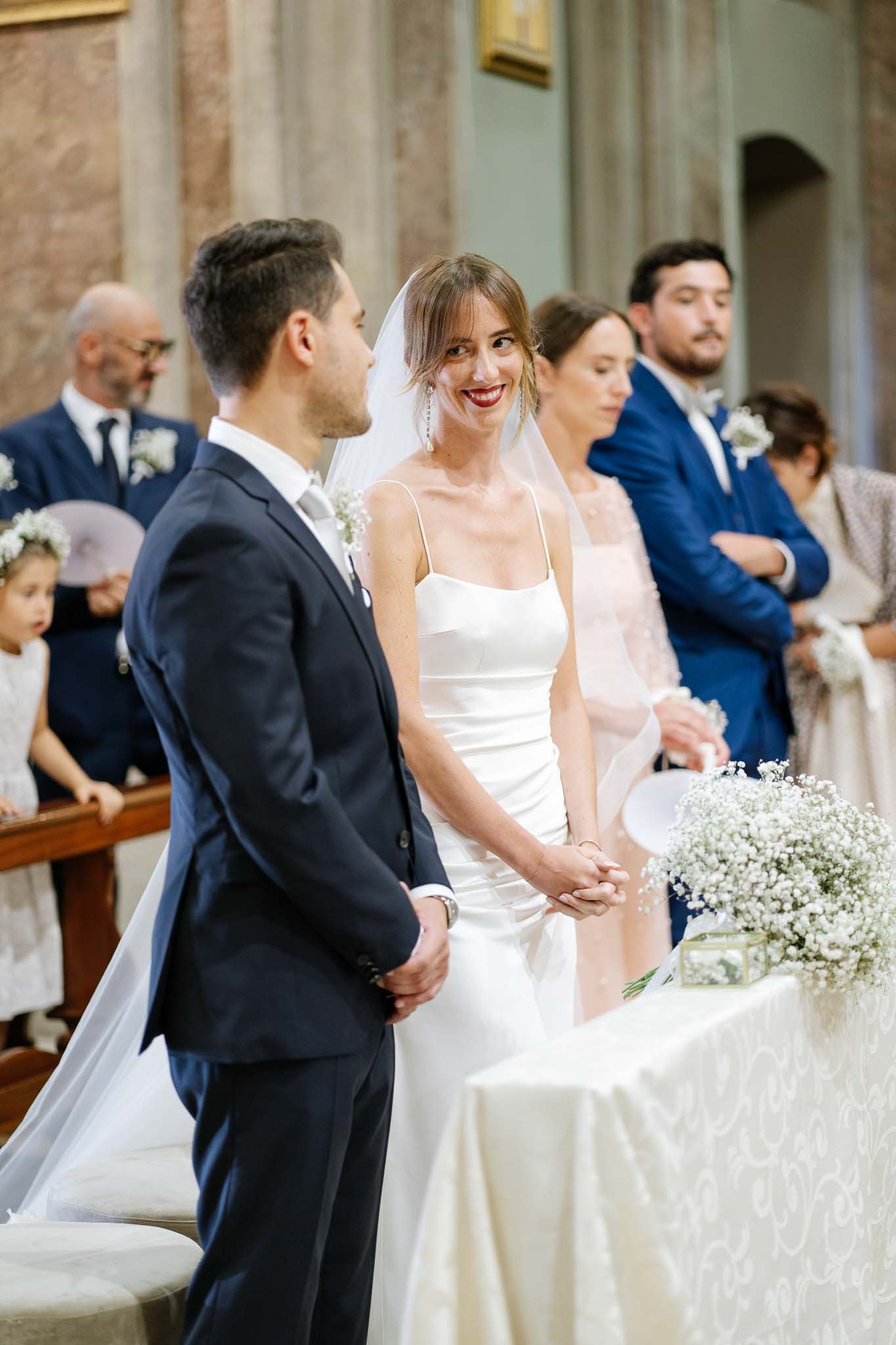 Elegant couple at church altar during wedding ceremony with white floral decorations.