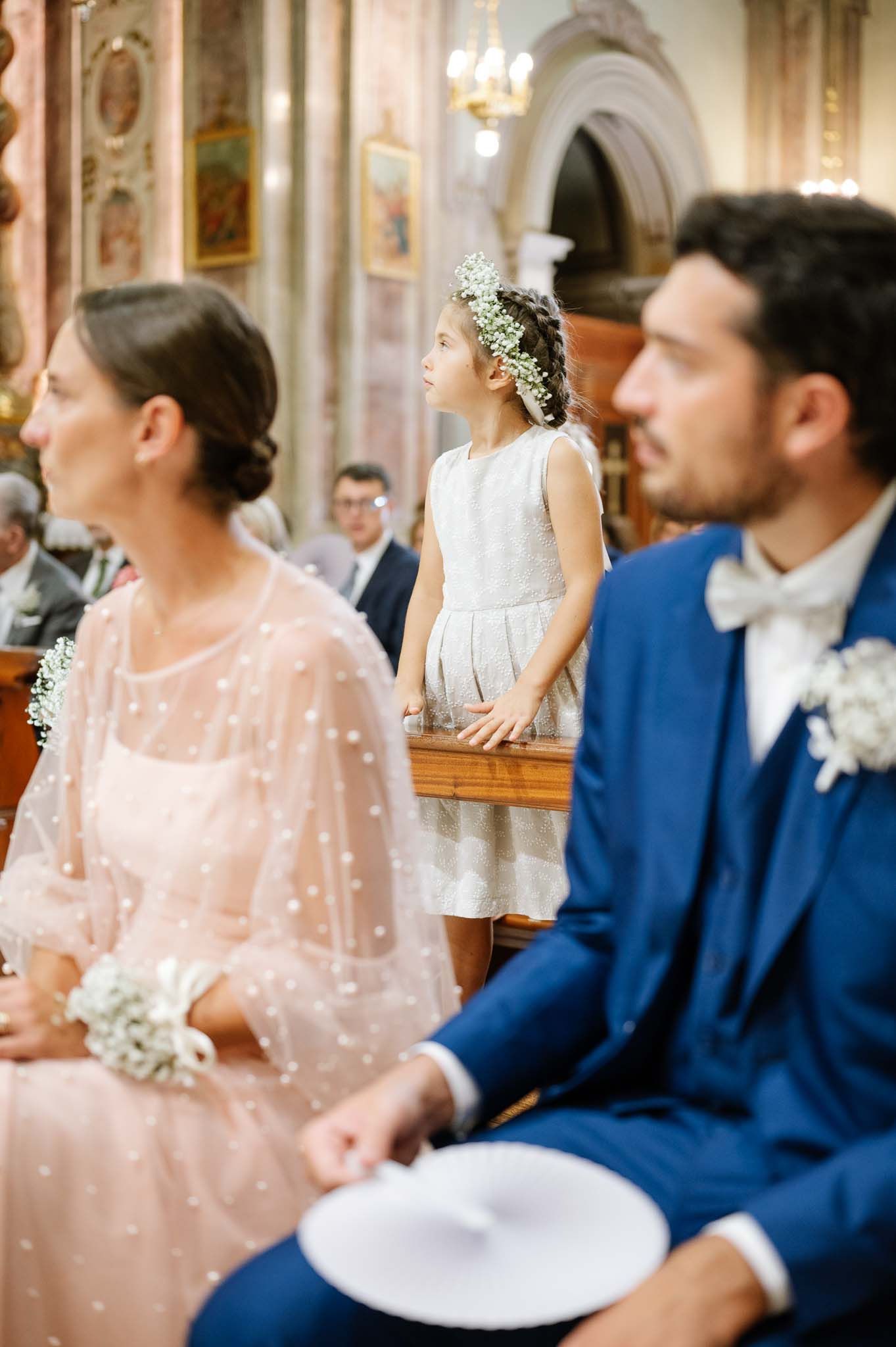 Wedding attendees in formal attire gathered in church pews with decorative architecture visible.