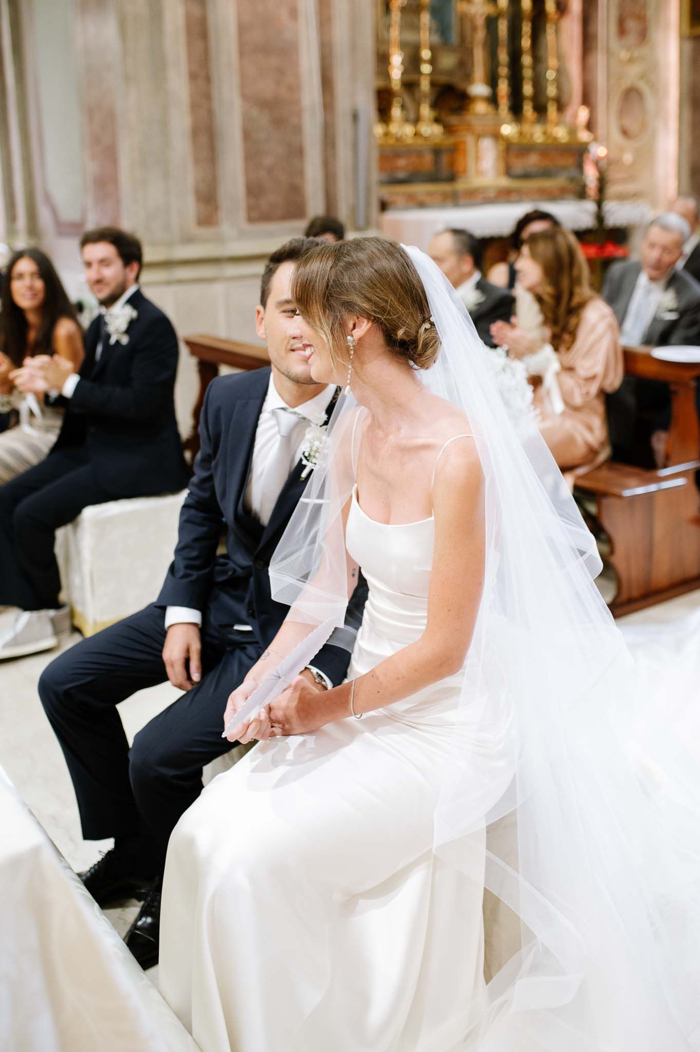 Couple seated during wedding ceremony in an ornate church with decorative marble columns.