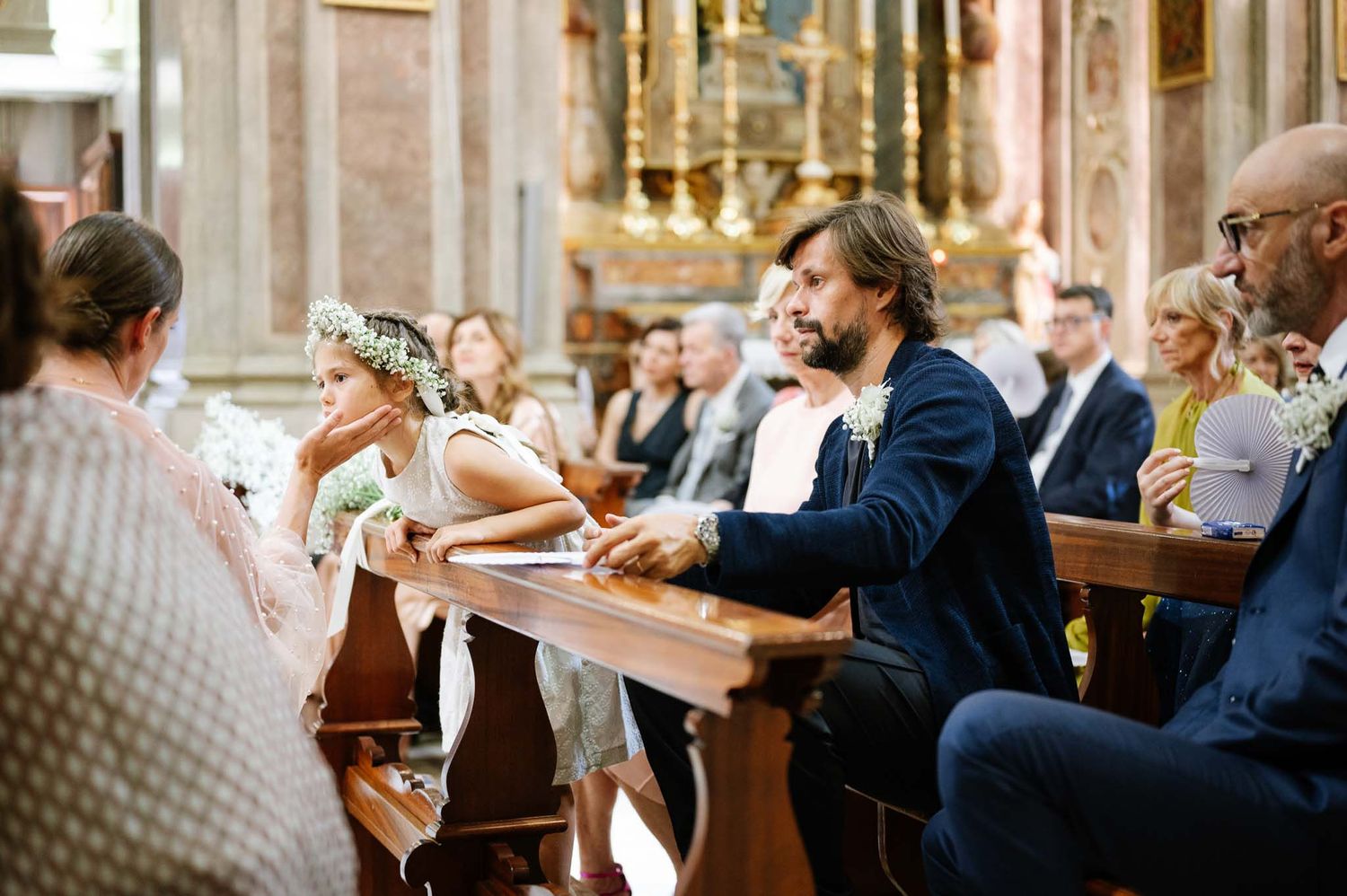 Guests are seated in church pews during a wedding ceremony in an ornate traditional church.