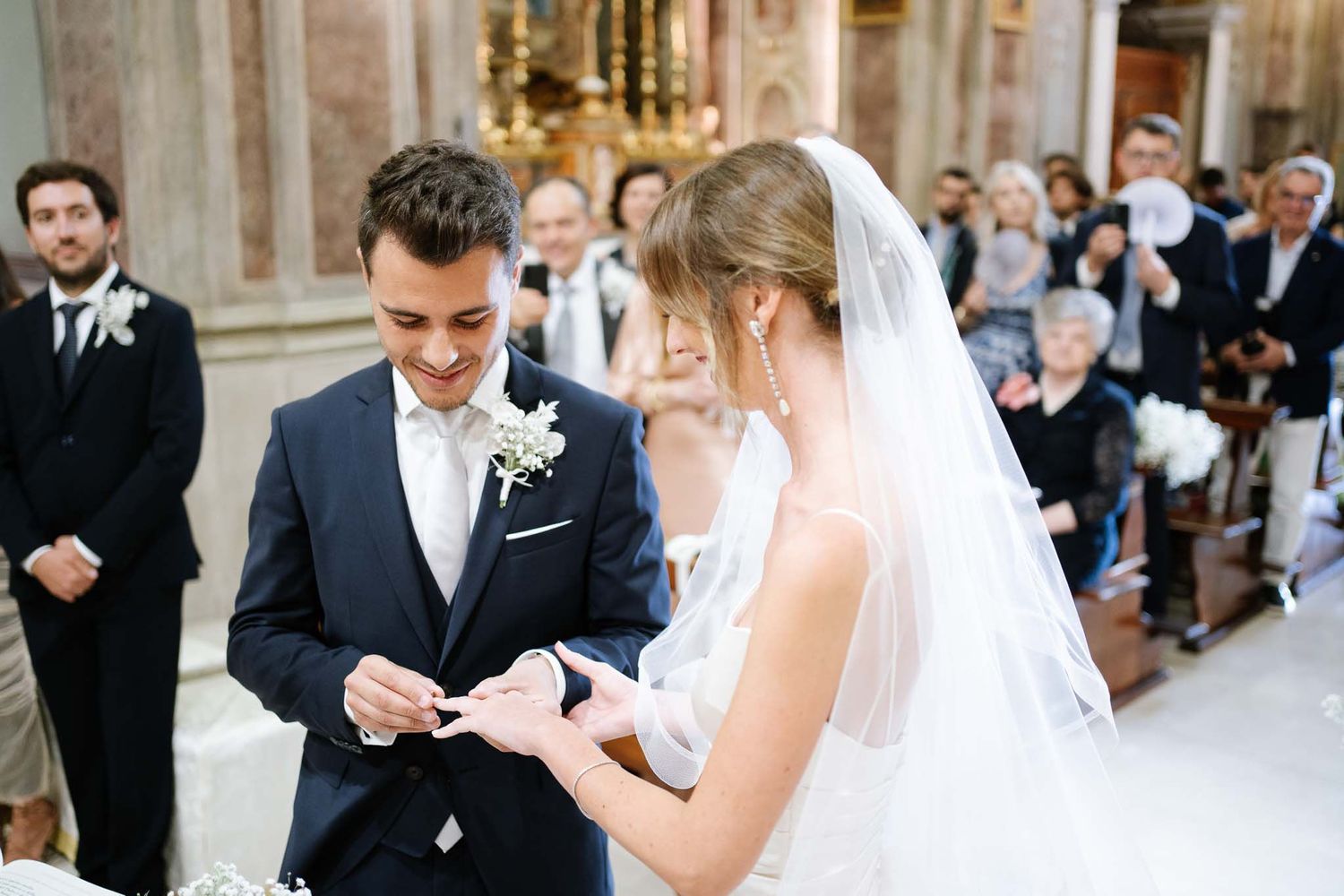 Wedding ceremony in progress showing ring exchange in an elegant church setting.
