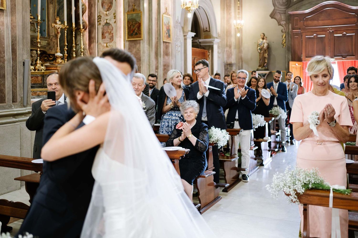 Guests watch emotionally during an intimate church wedding ceremony with elegant candles and floral decorations.