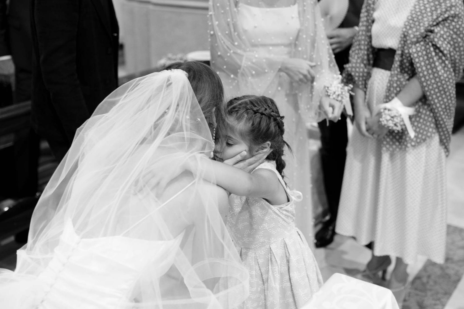 A touching black and white moment as a bride in her wedding gown embraces a young guest.