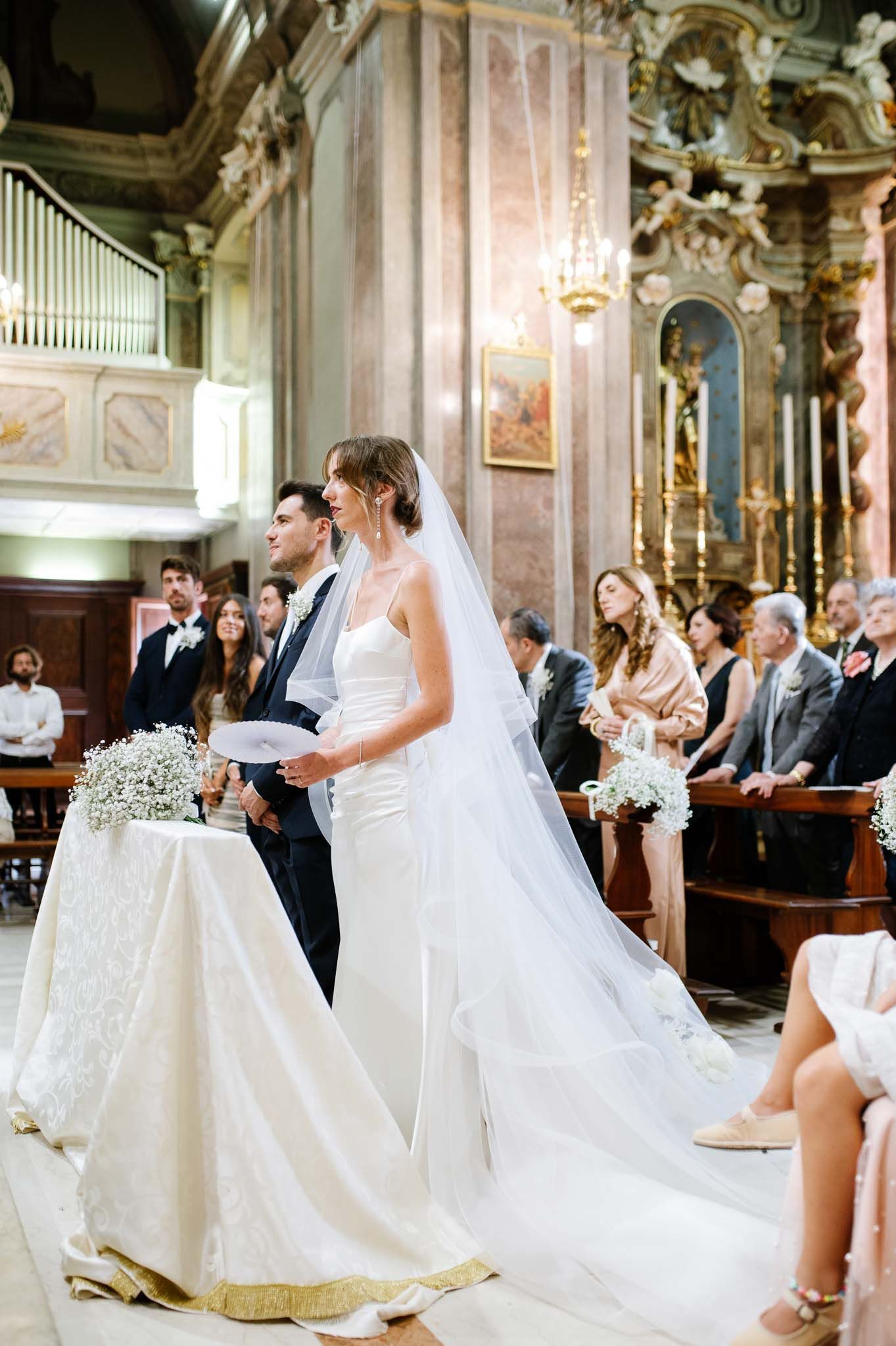 A couple stands at the altar in an ornate church with beautiful baroque architecture and decorative elements.