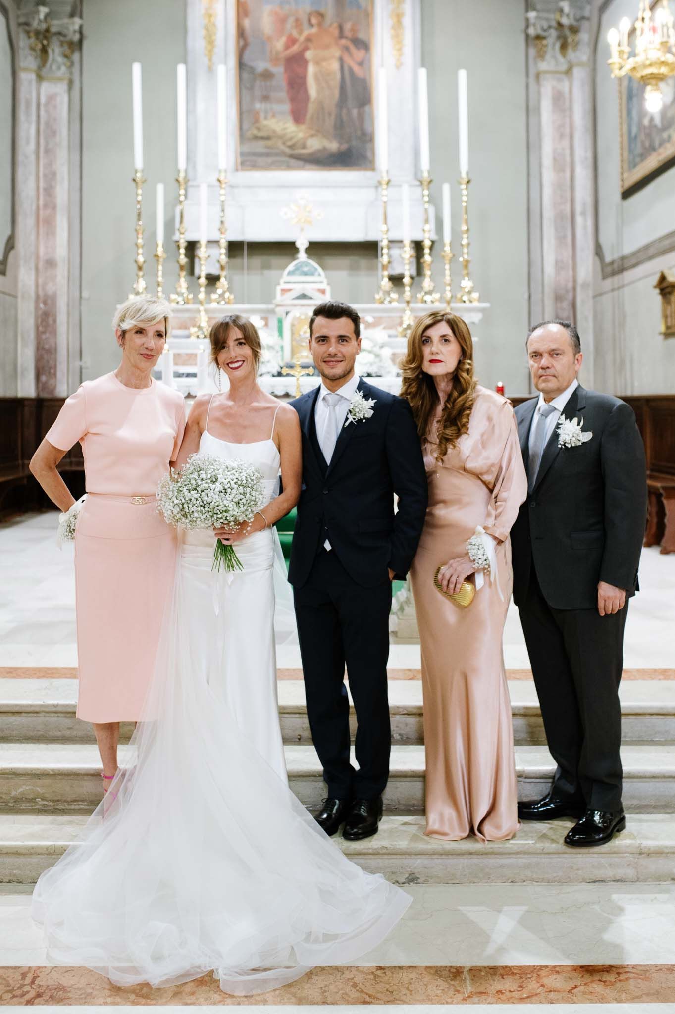 Wedding party poses formally in front of church altar with elegant candelabras and religious artwork.