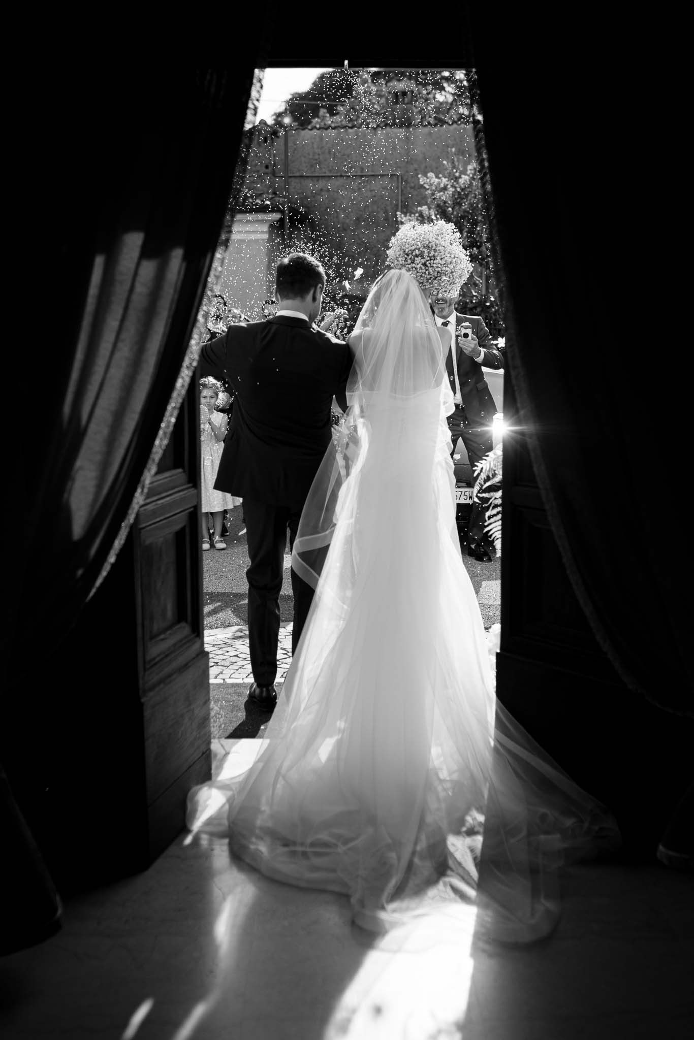 Black and white photo showing a couple in wedding attire silhouetted in a doorway at their ceremony.