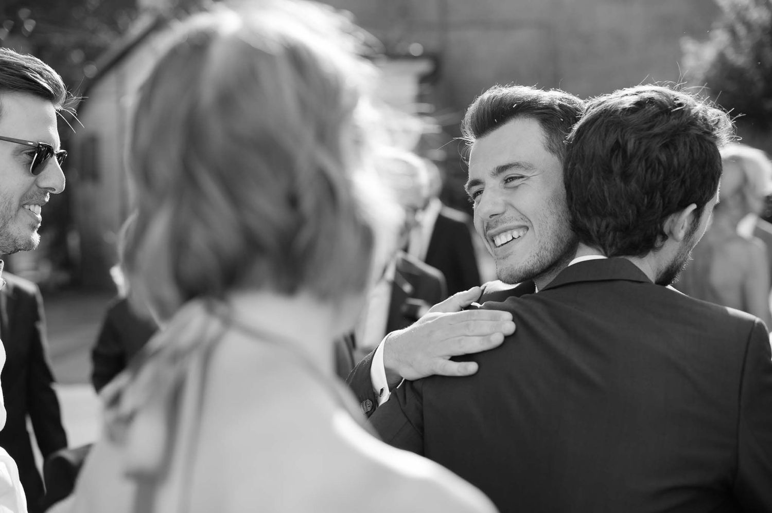 Joyful wedding guests embracing and laughing together during outdoor celebration.