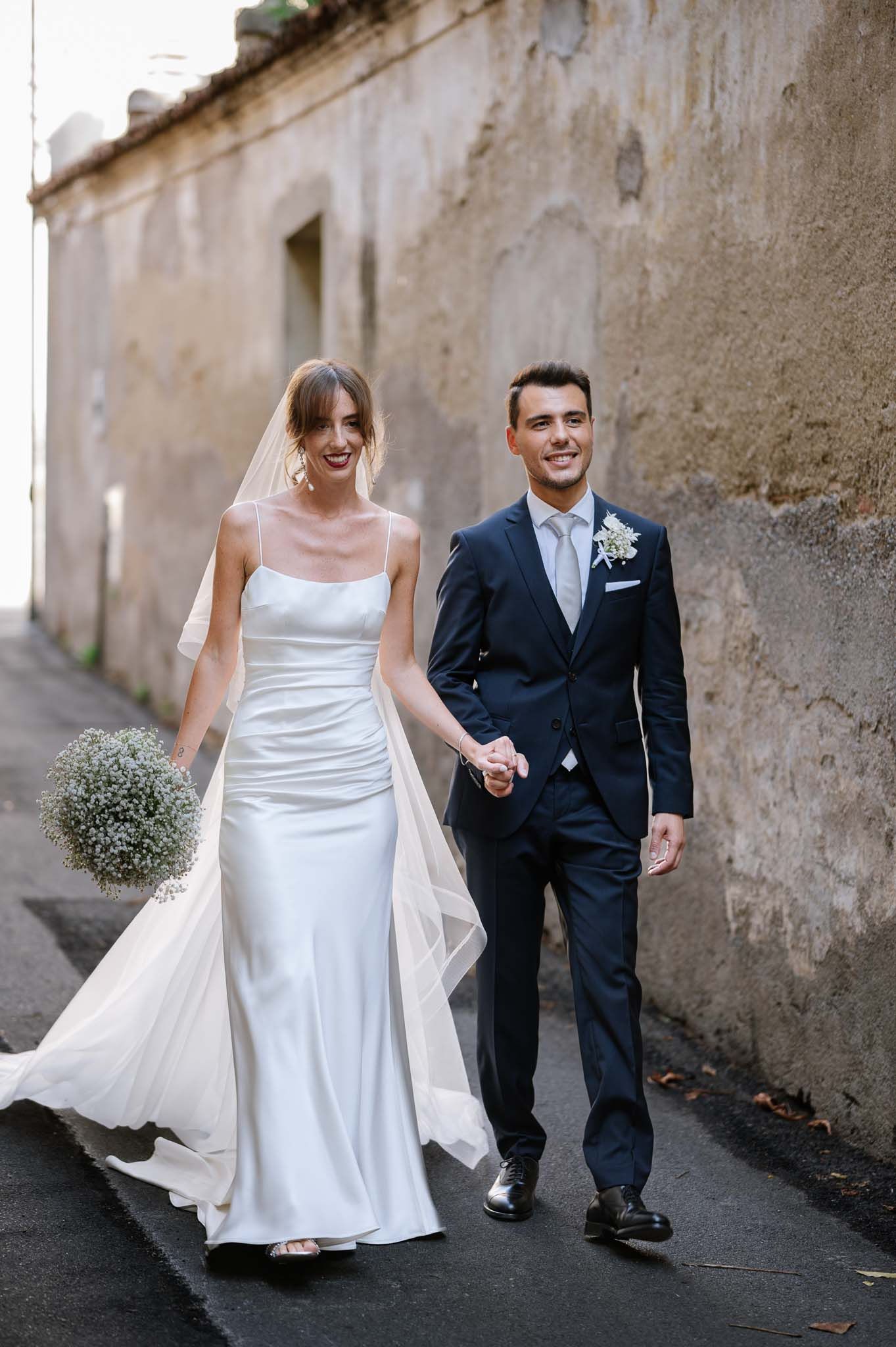 Wedding couple walking together on stone street with flowing bridal veil.