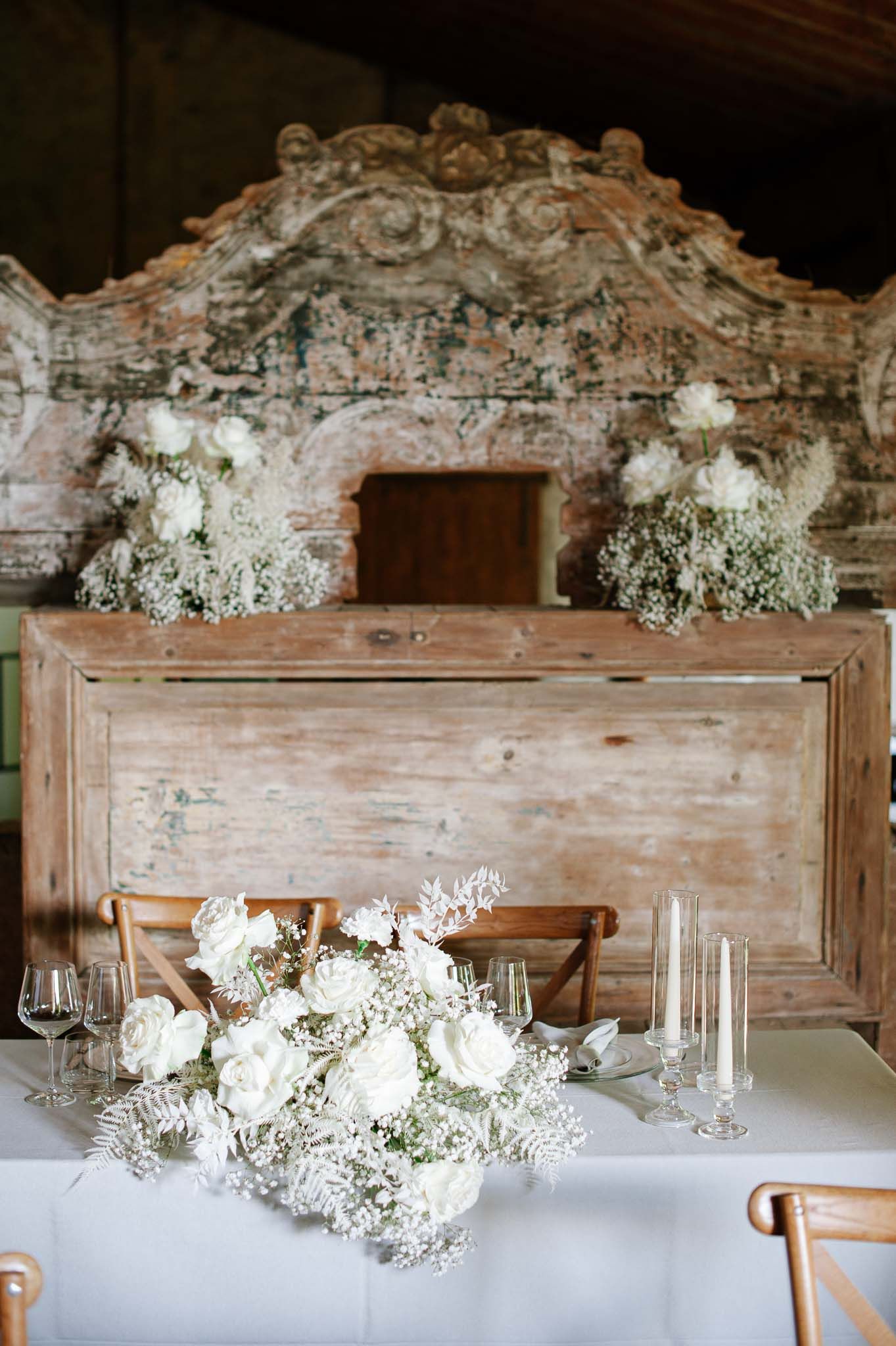 Rustic wedding table setting with white floral arrangements and a vintage wooden backdrop.