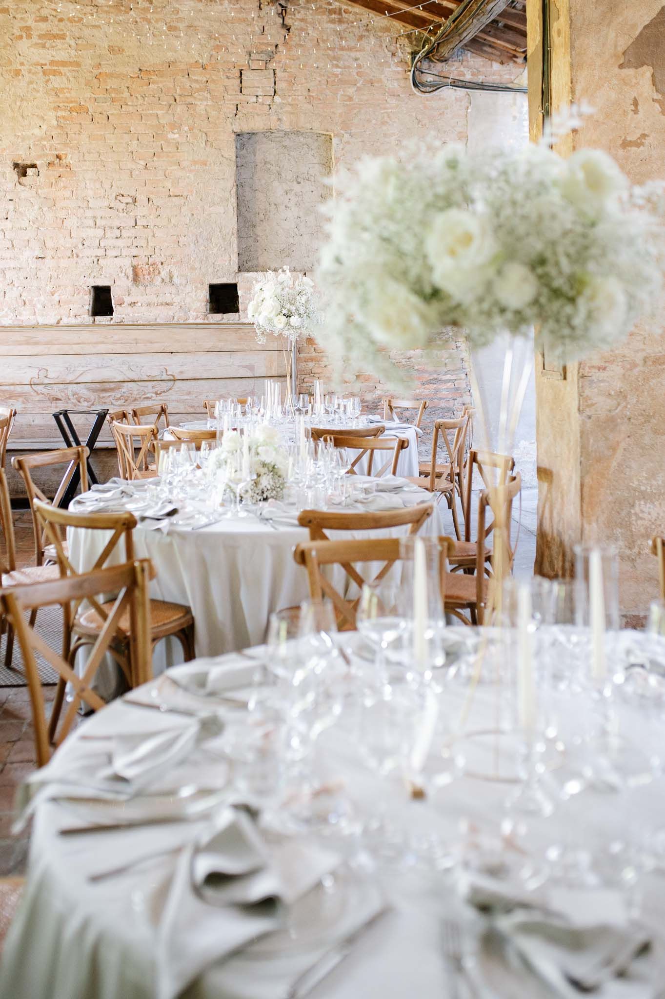 White table settings in a rustic brick venue with tall floral centerpieces.