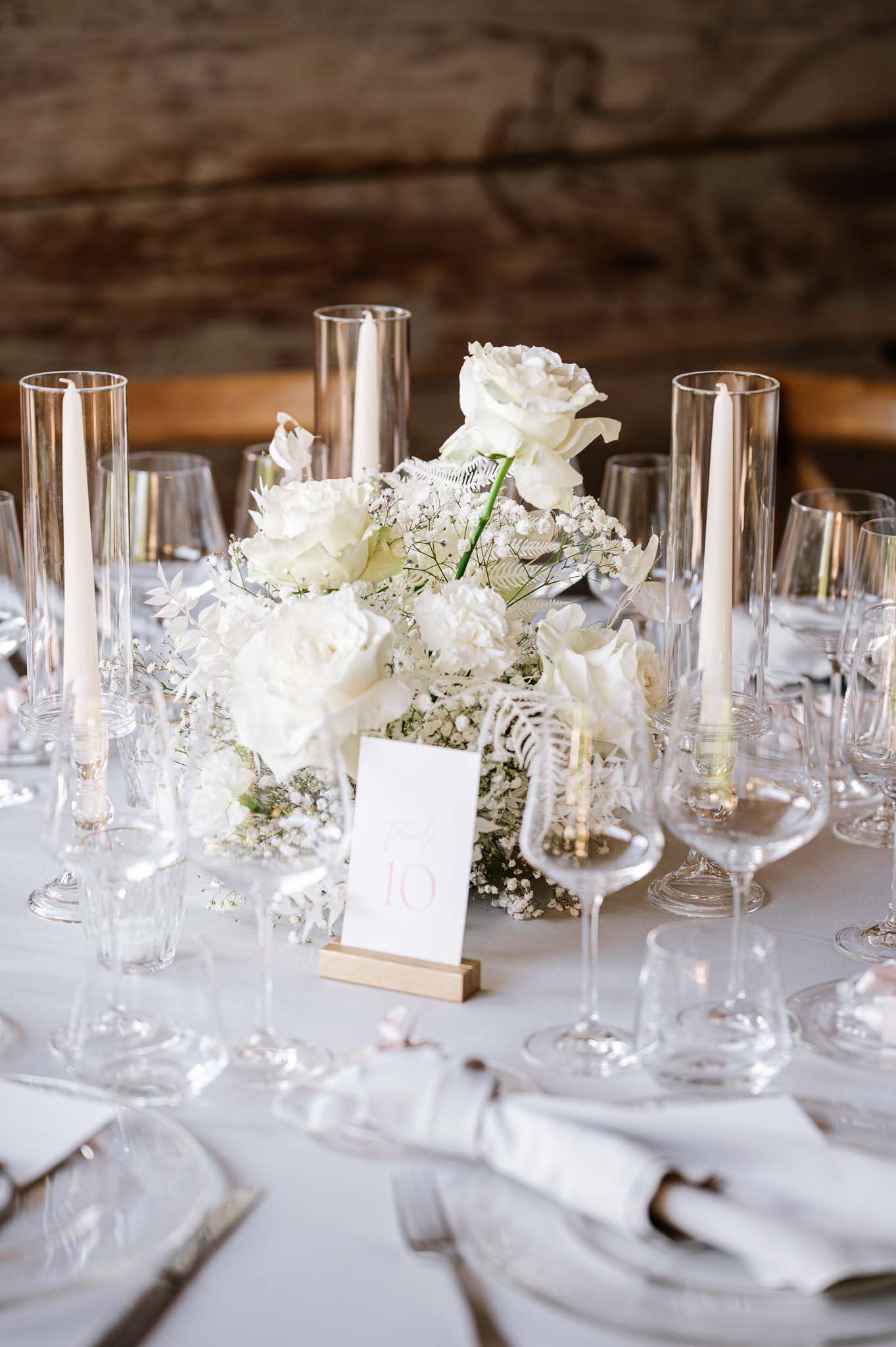Elegant table setting with white roses and baby's breath centerpiece surrounded by crystal glasses.