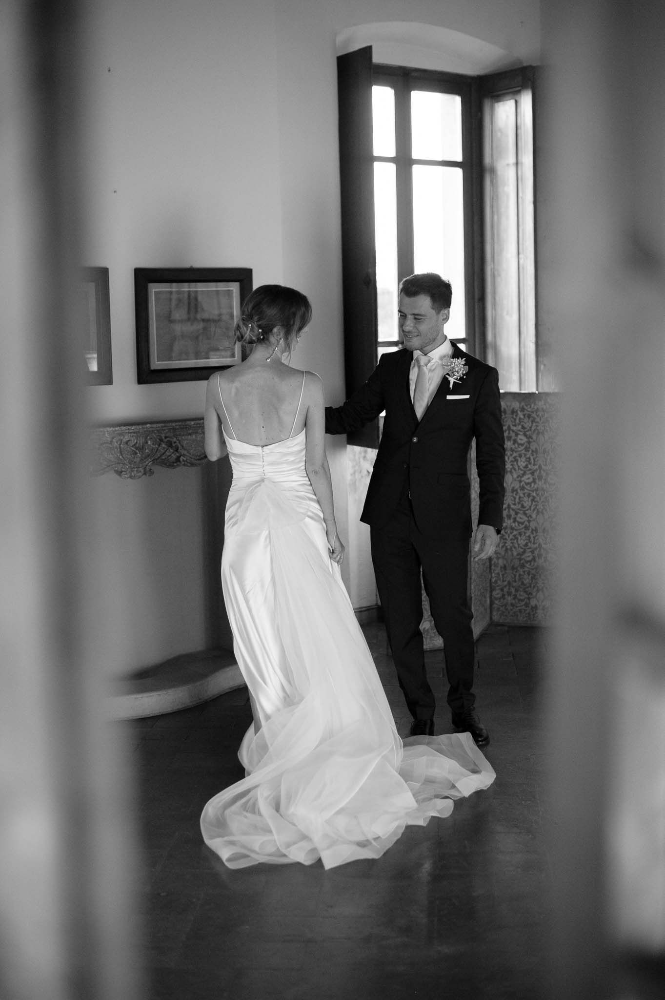 A romantic black and white wedding photo of a couple standing in an elegant hallway with natural light.