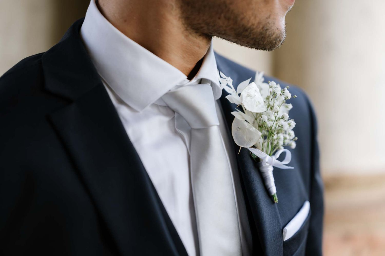 Close up detail of a white boutonniere on a black tuxedo lapel with crisp white shirt collar.
