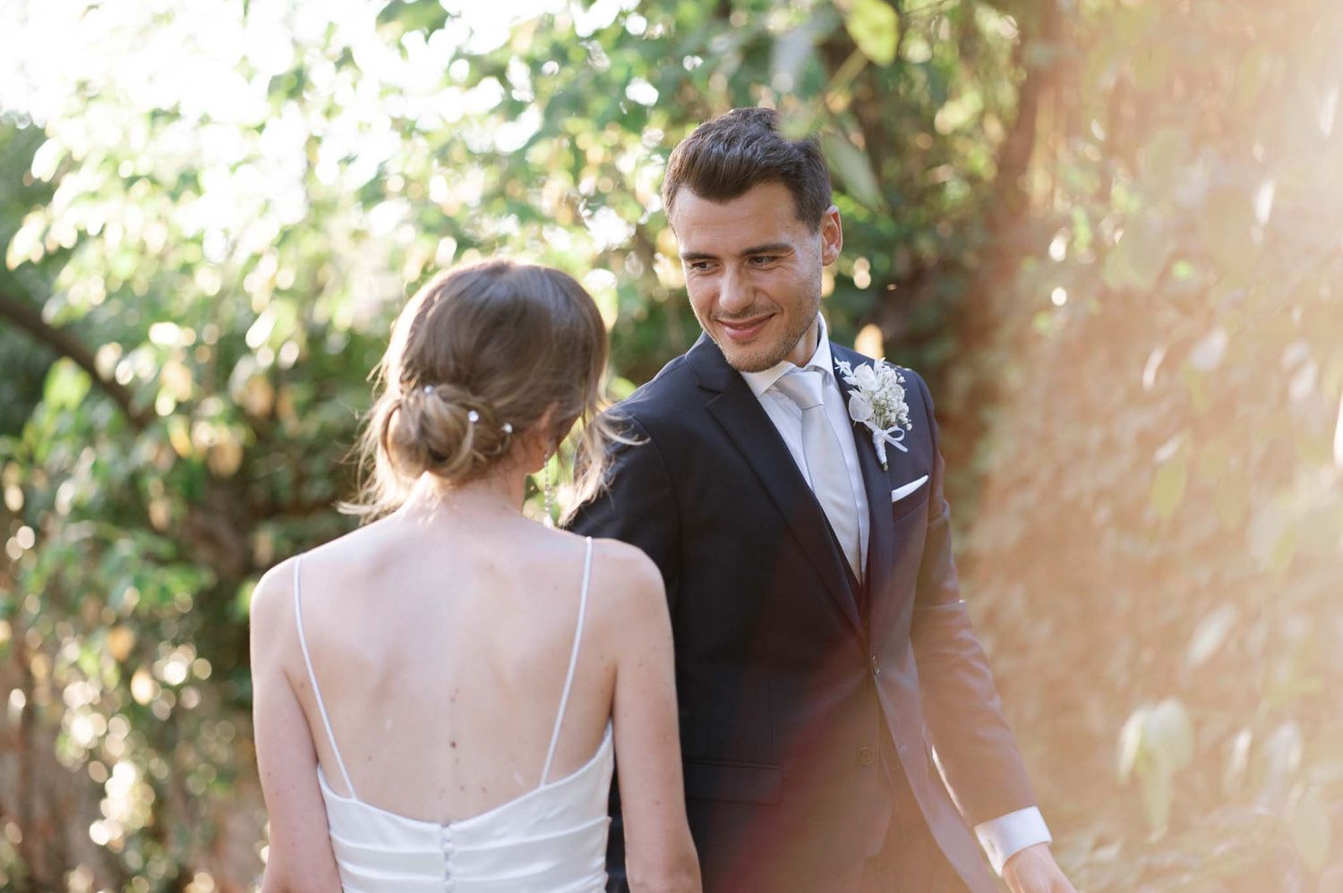 Newlyweds share tender moment in sunlit garden setting during wedding portraits.