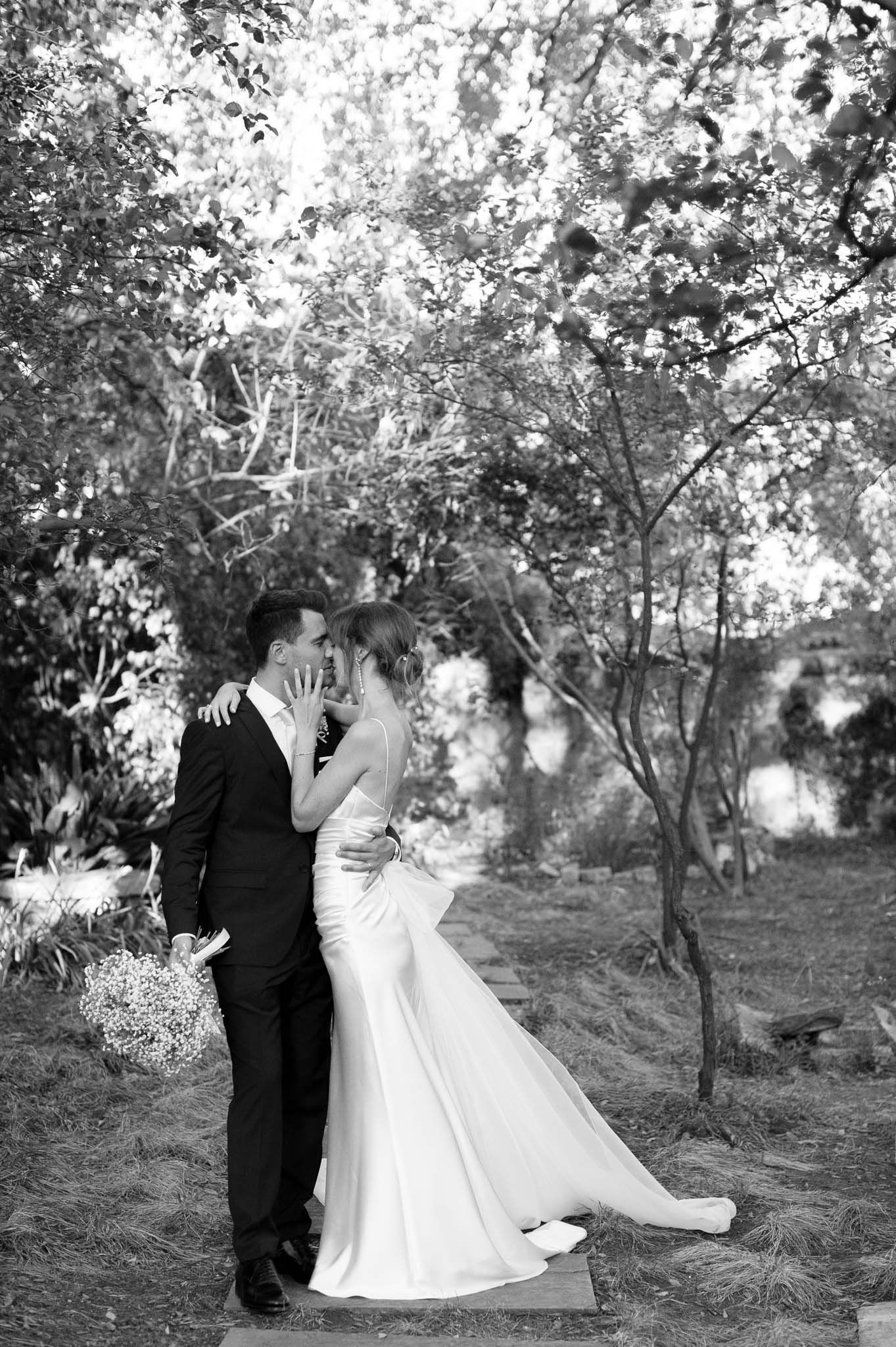 Black and white portrait of newlyweds embracing in garden with baby's breath bouquet.