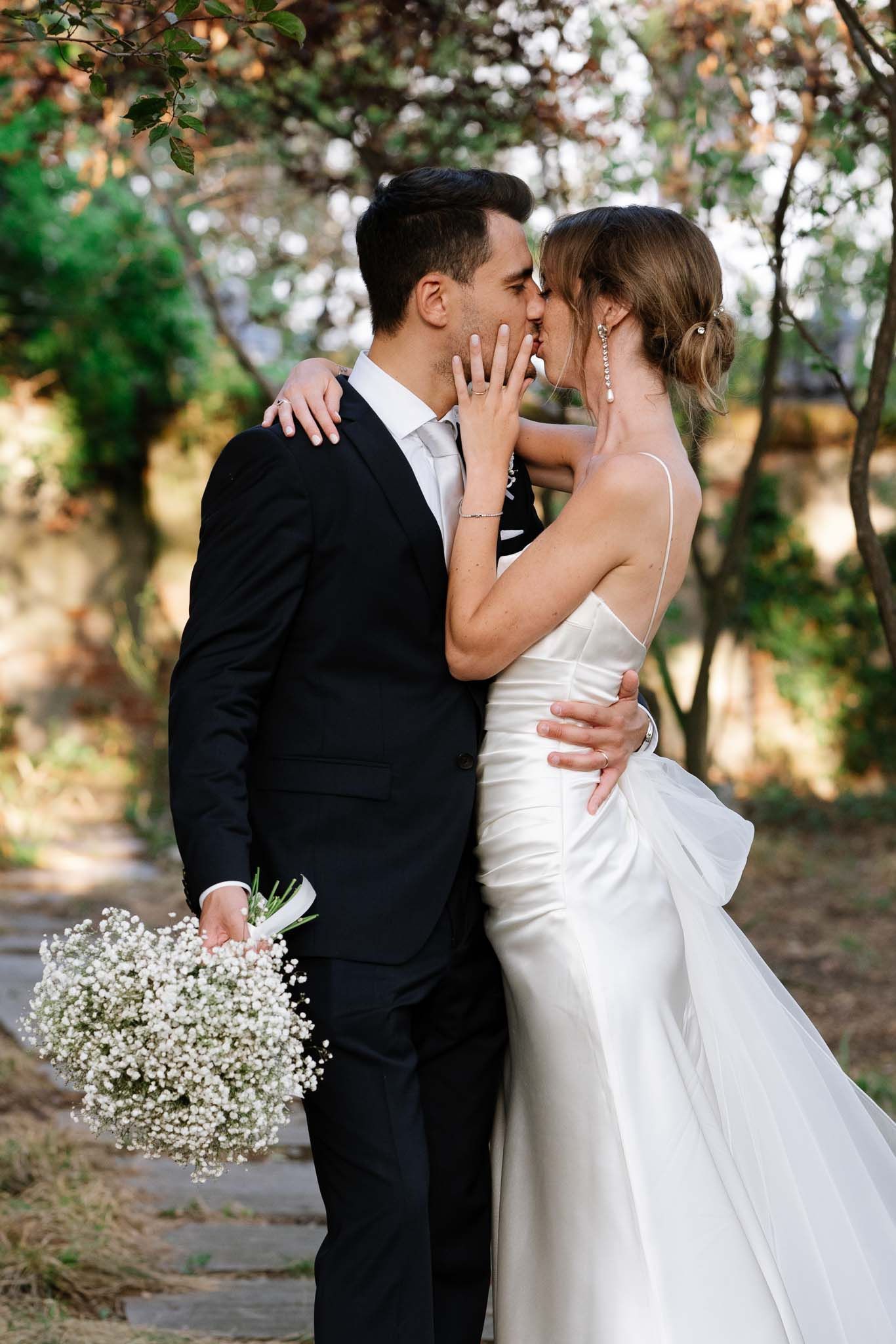 Intimate moment between newlyweds with baby's breath bouquet in garden setting.
