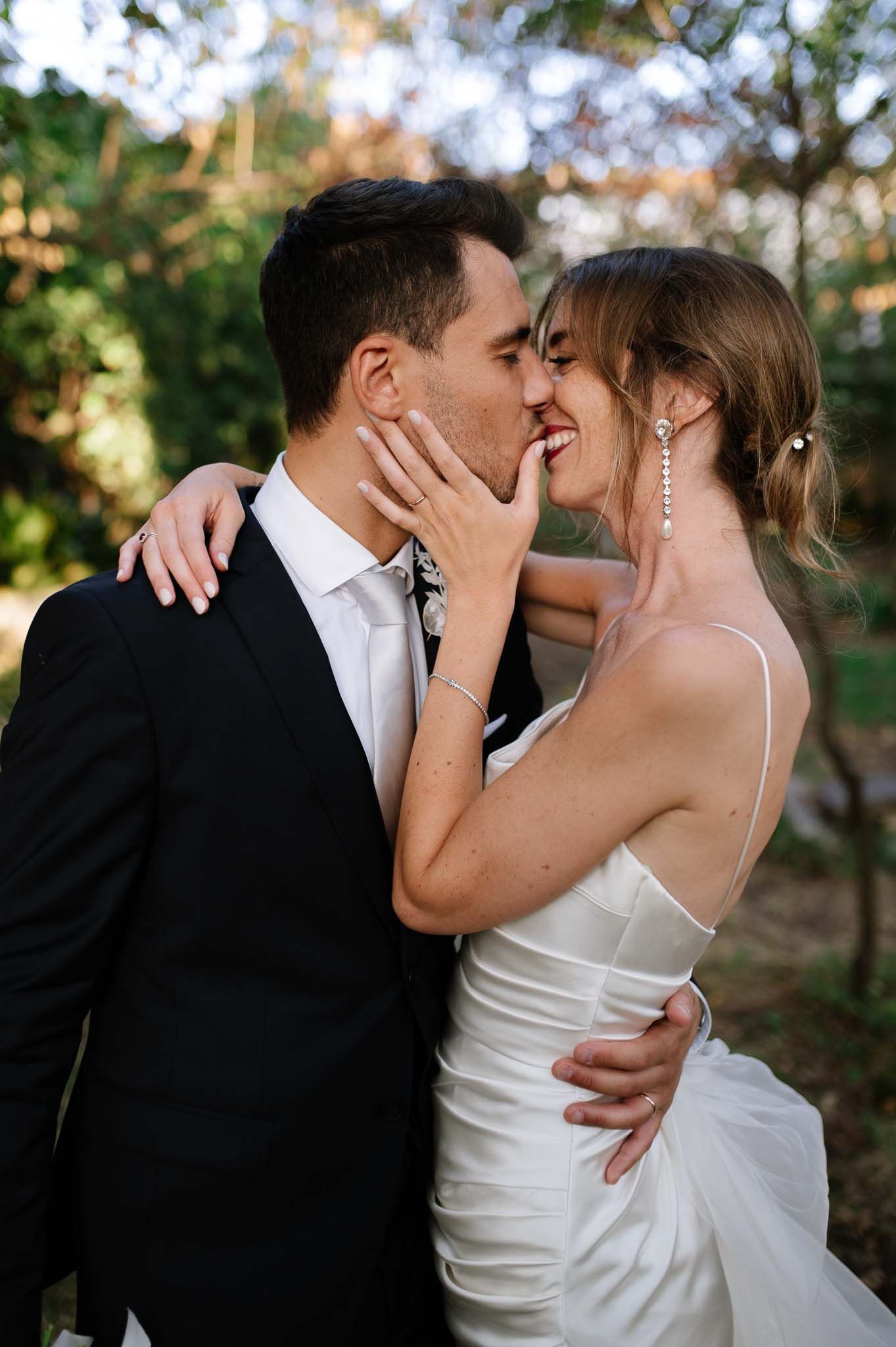 Romantic outdoor wedding portrait of a couple sharing an intimate kiss in formal attire.