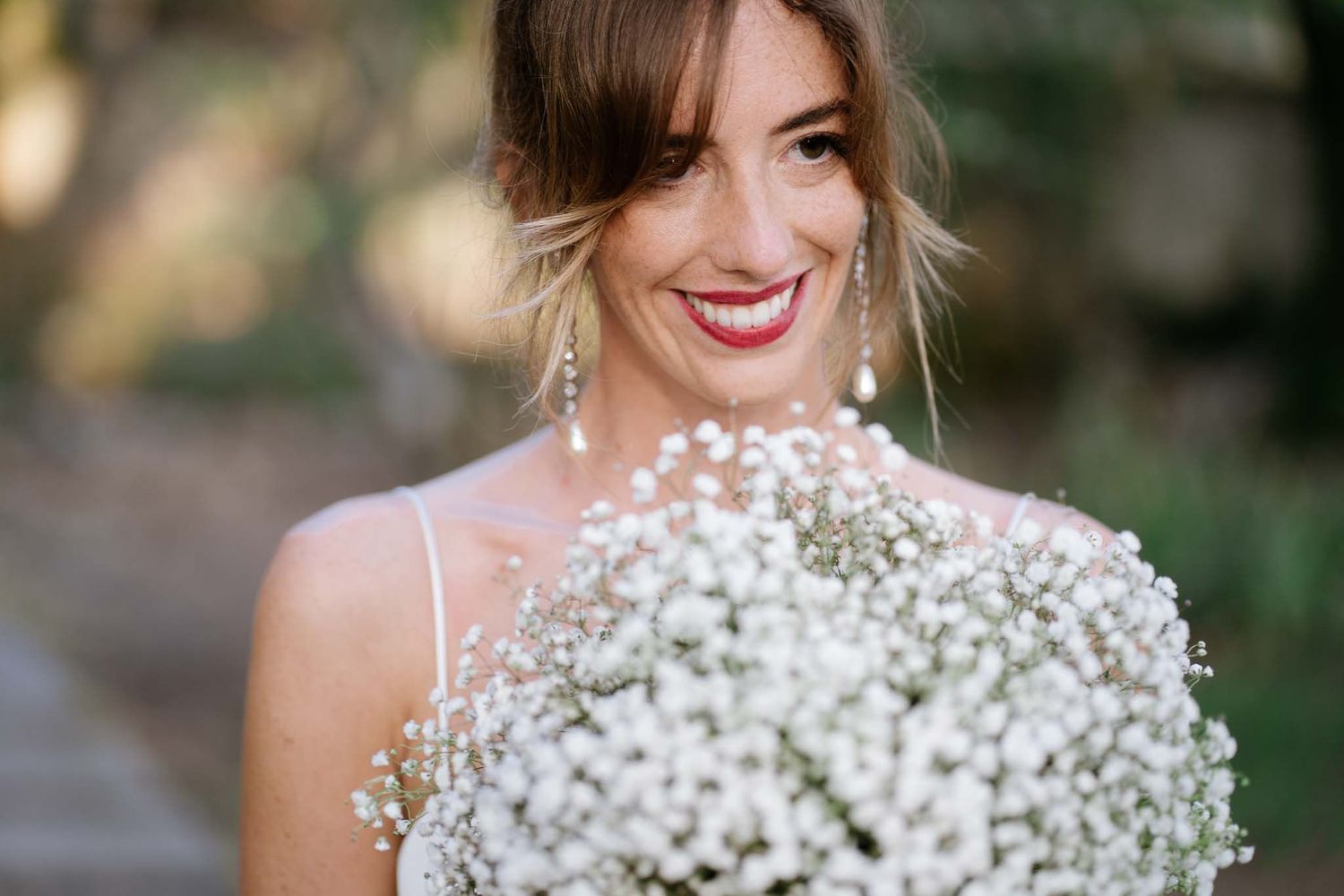 Joyful bride holding a stunning bouquet of white baby's breath flowers with natural garden backdrop.