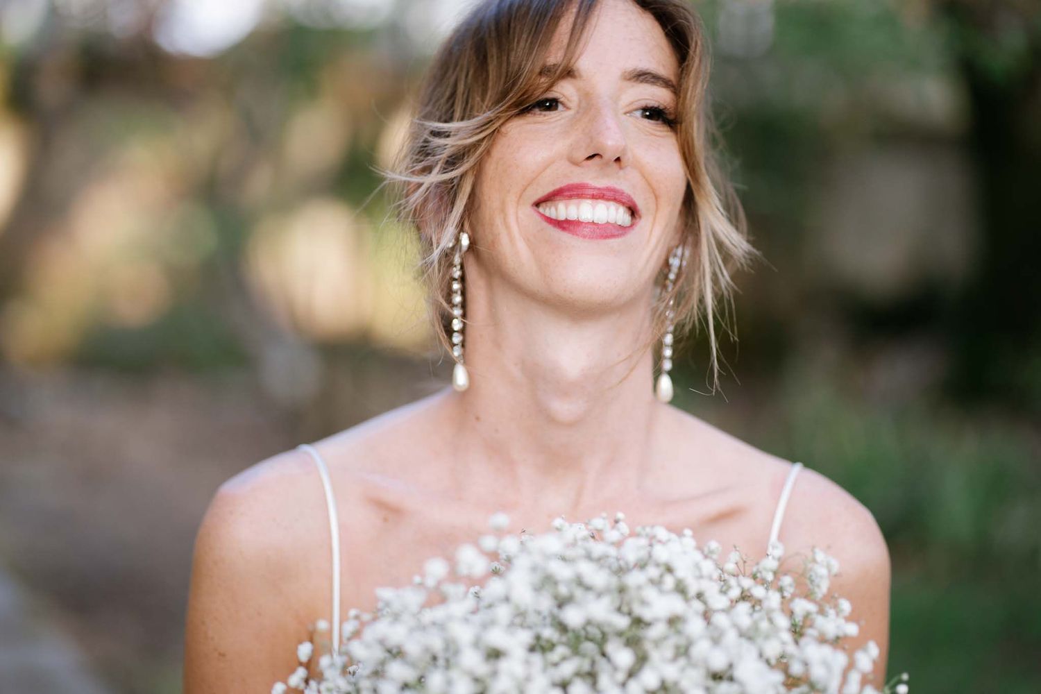 Candid portrait of bride laughing while holding white baby's breath bouquet outdoors.