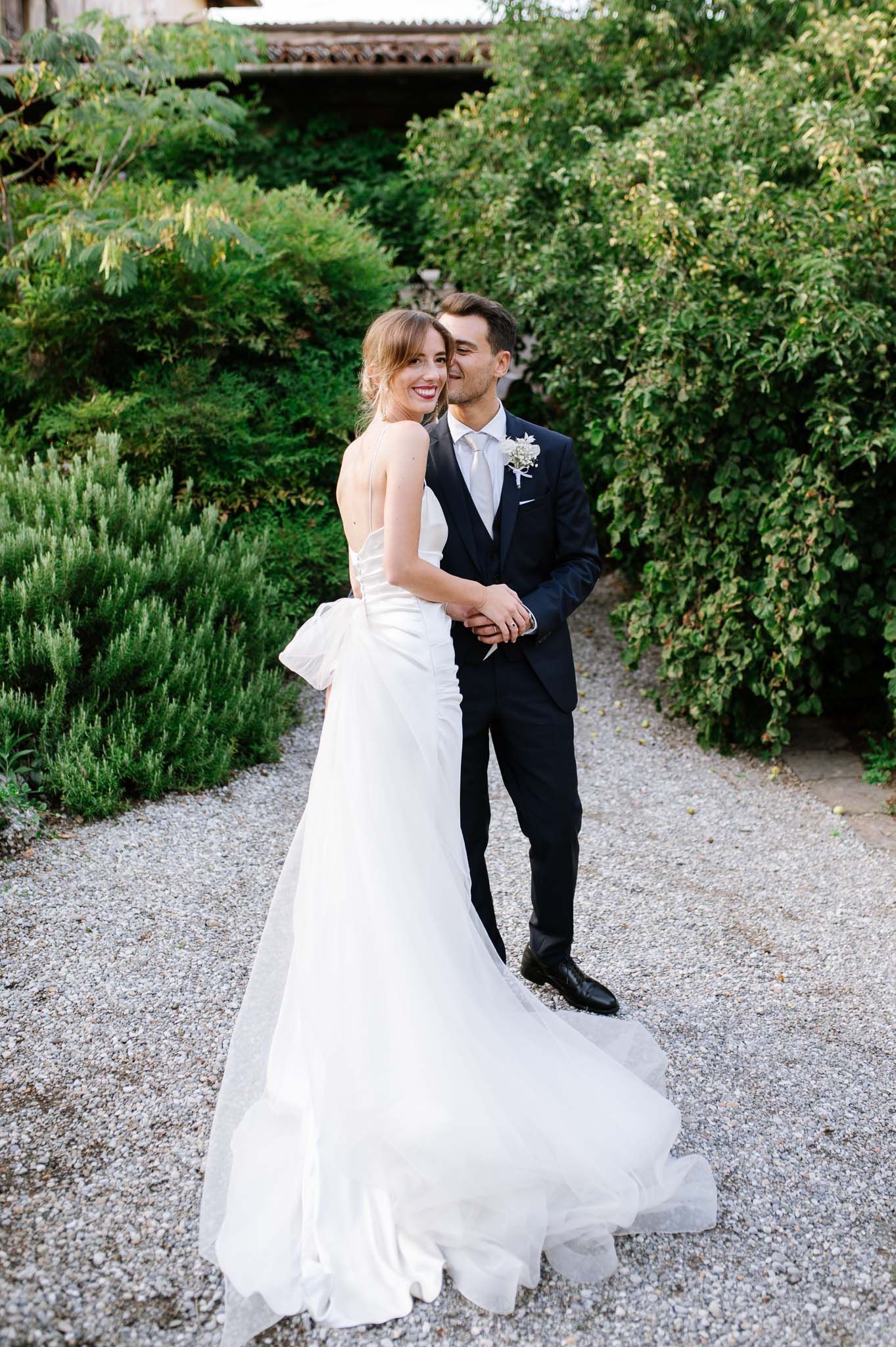 Full-length wedding portrait of couple on garden path with flowing white bridal gown.