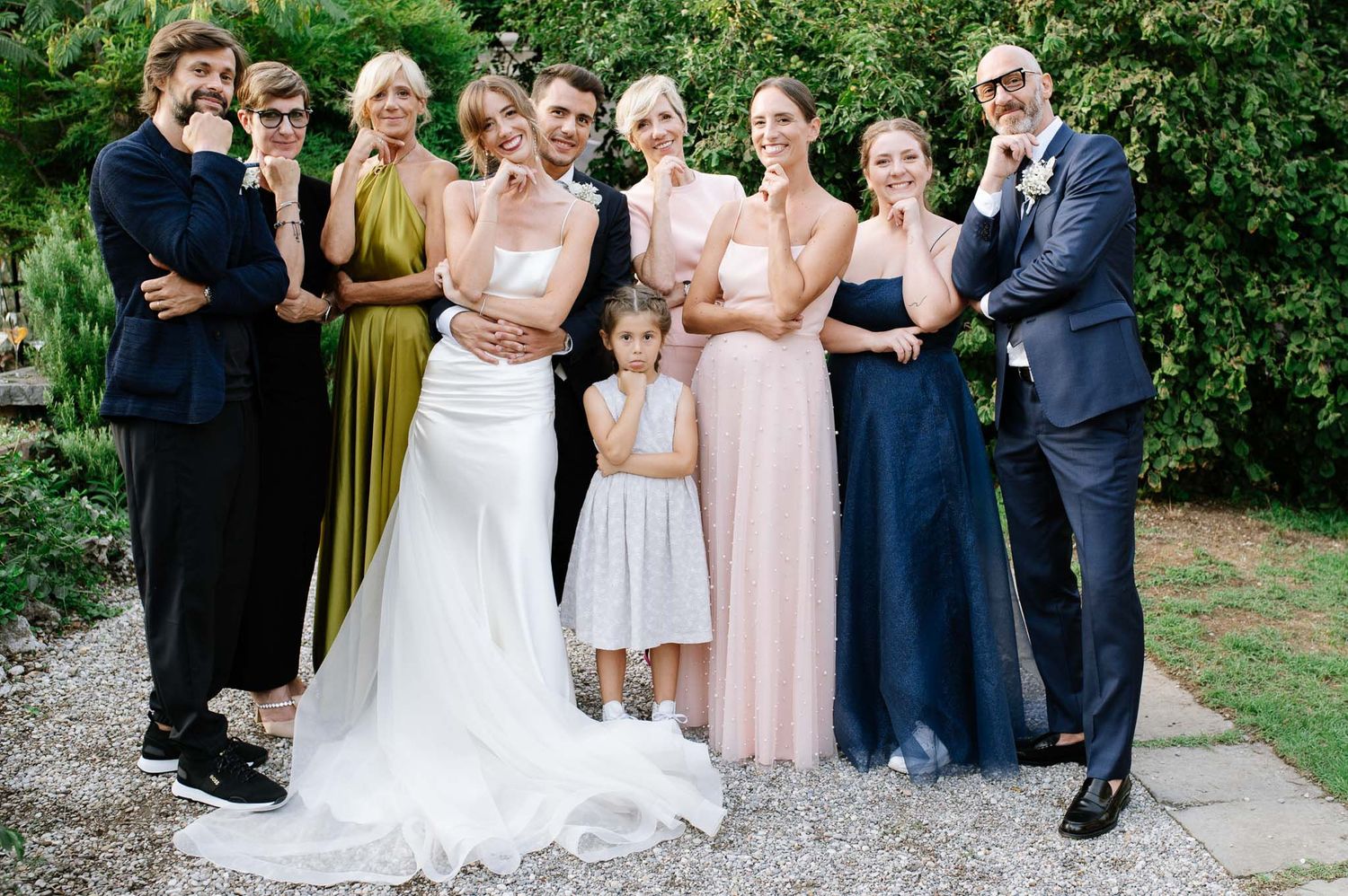 Wedding party group photo with bridesmaids in mixed formal attire on garden path.