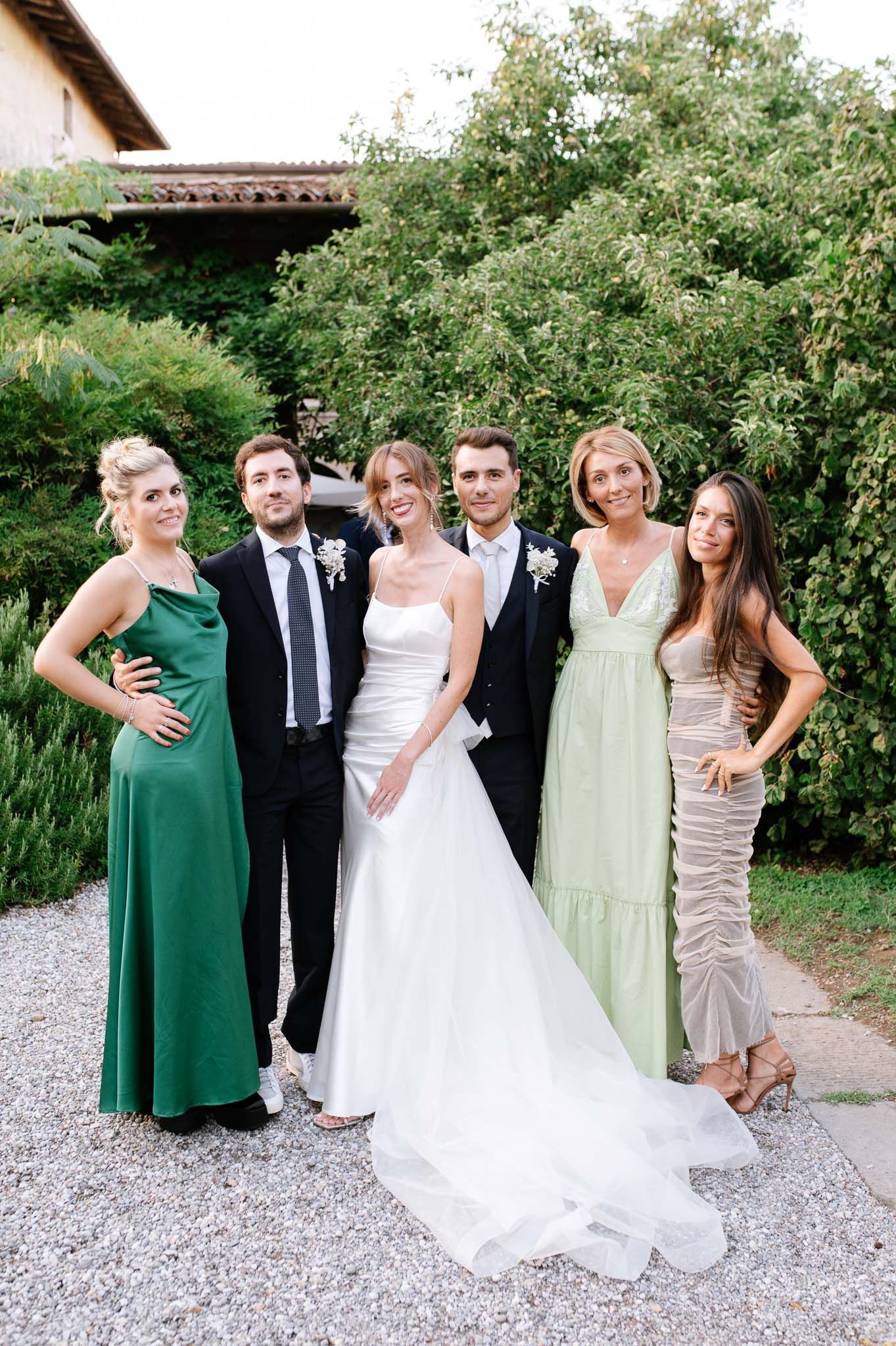 Wedding party portrait featuring bridal party in coordinated formal dresses against garden setting.