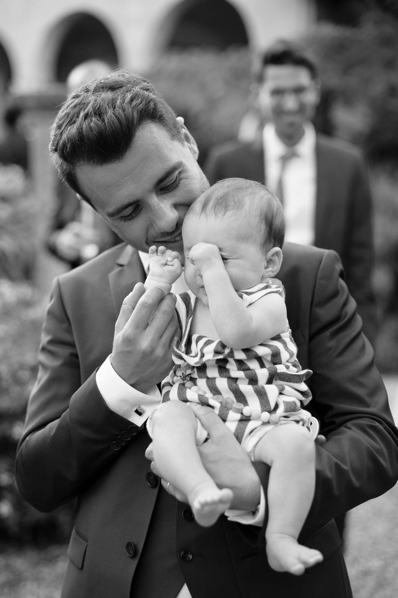 A tender moment between a suited guest and a small baby at an outdoor event.