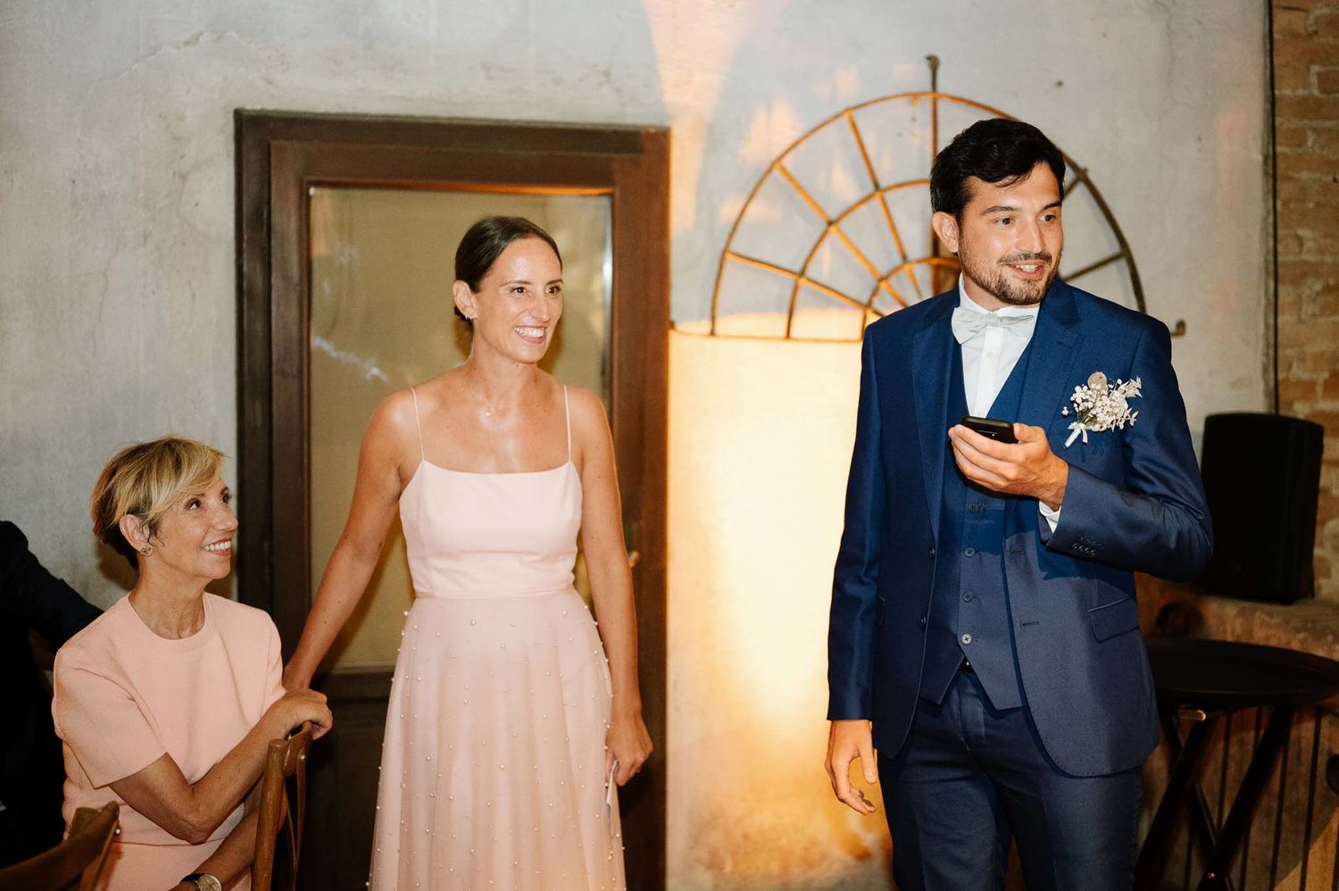 Wedding party members in formal attire entering a rustic venue space.