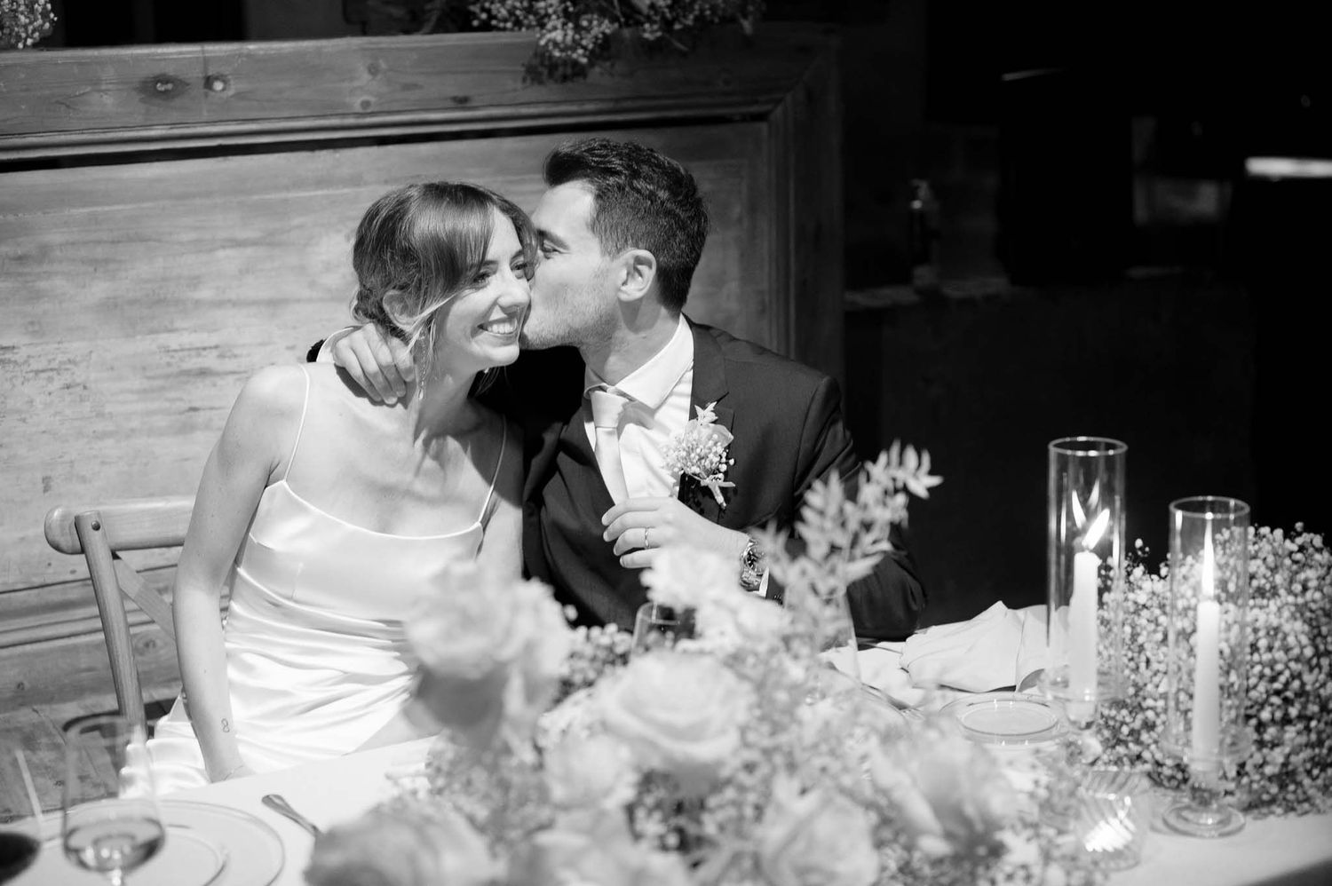 A romantic black and white wedding photo of a couple seated at a table with floral decorations.