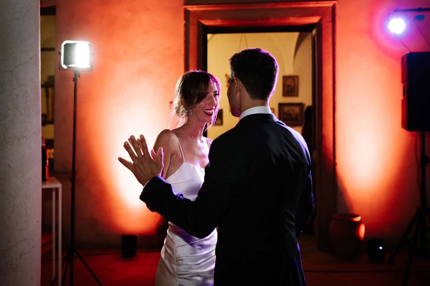 A couple shares an intimate dance moment in a room lit with warm red ambient lighting.