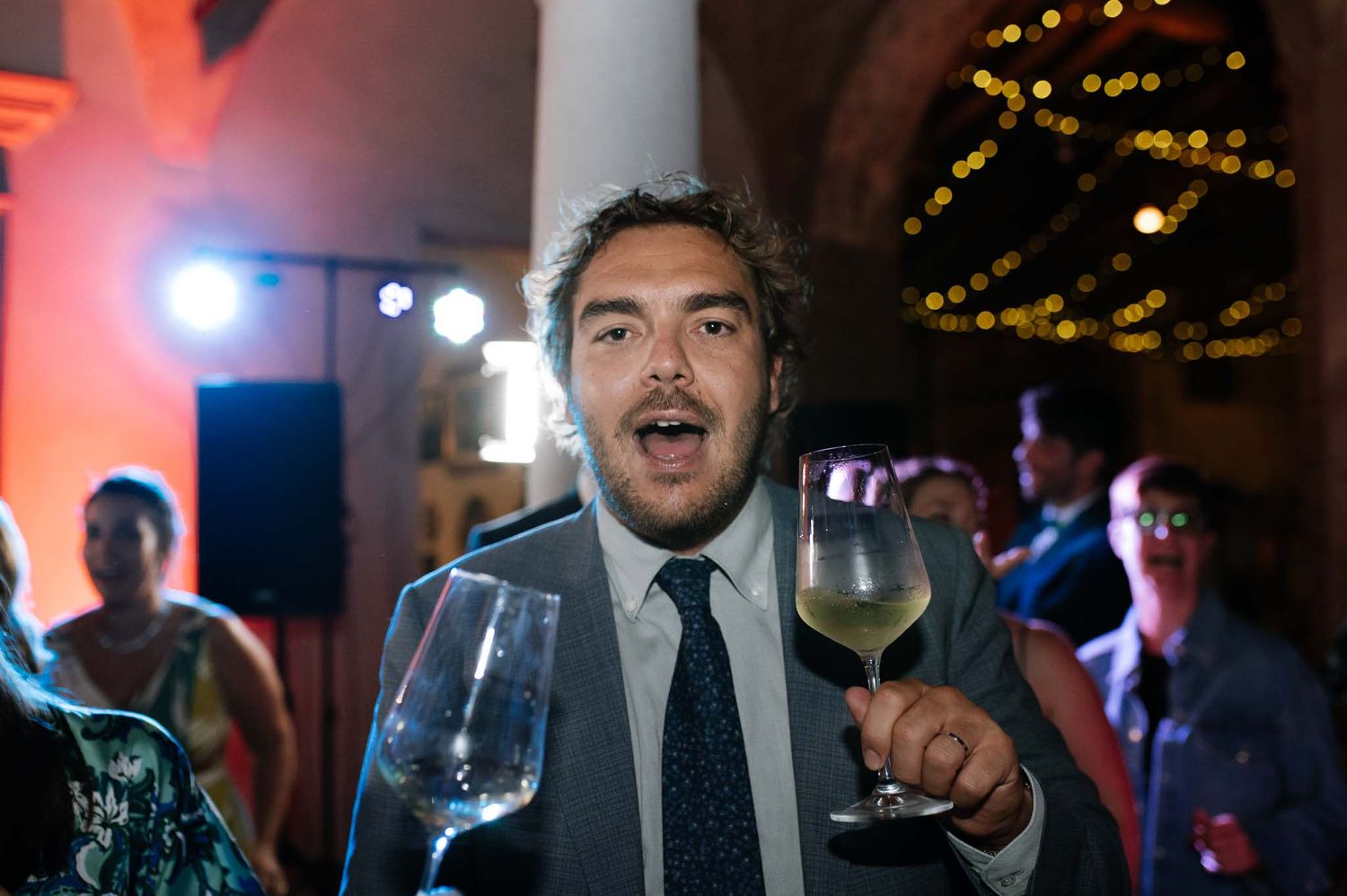 Party guest raising a wine glass in celebration with festive lighting in the background.