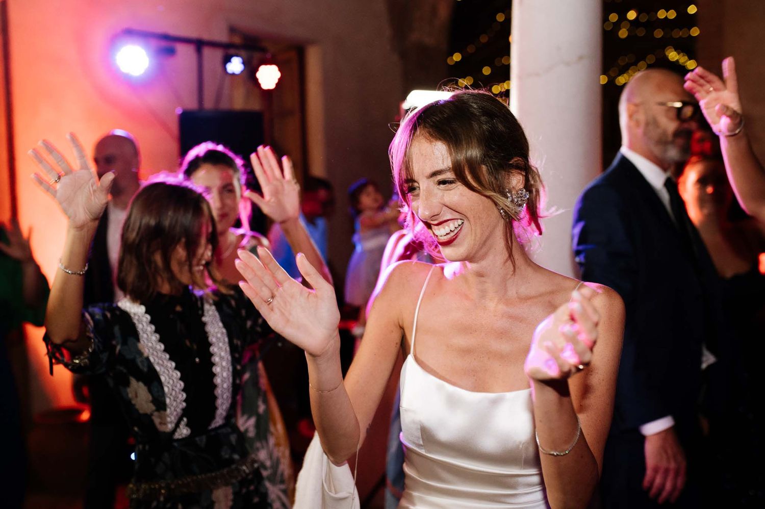 Celebratory dancing at a reception with vibrant mood lighting and architectural columns.