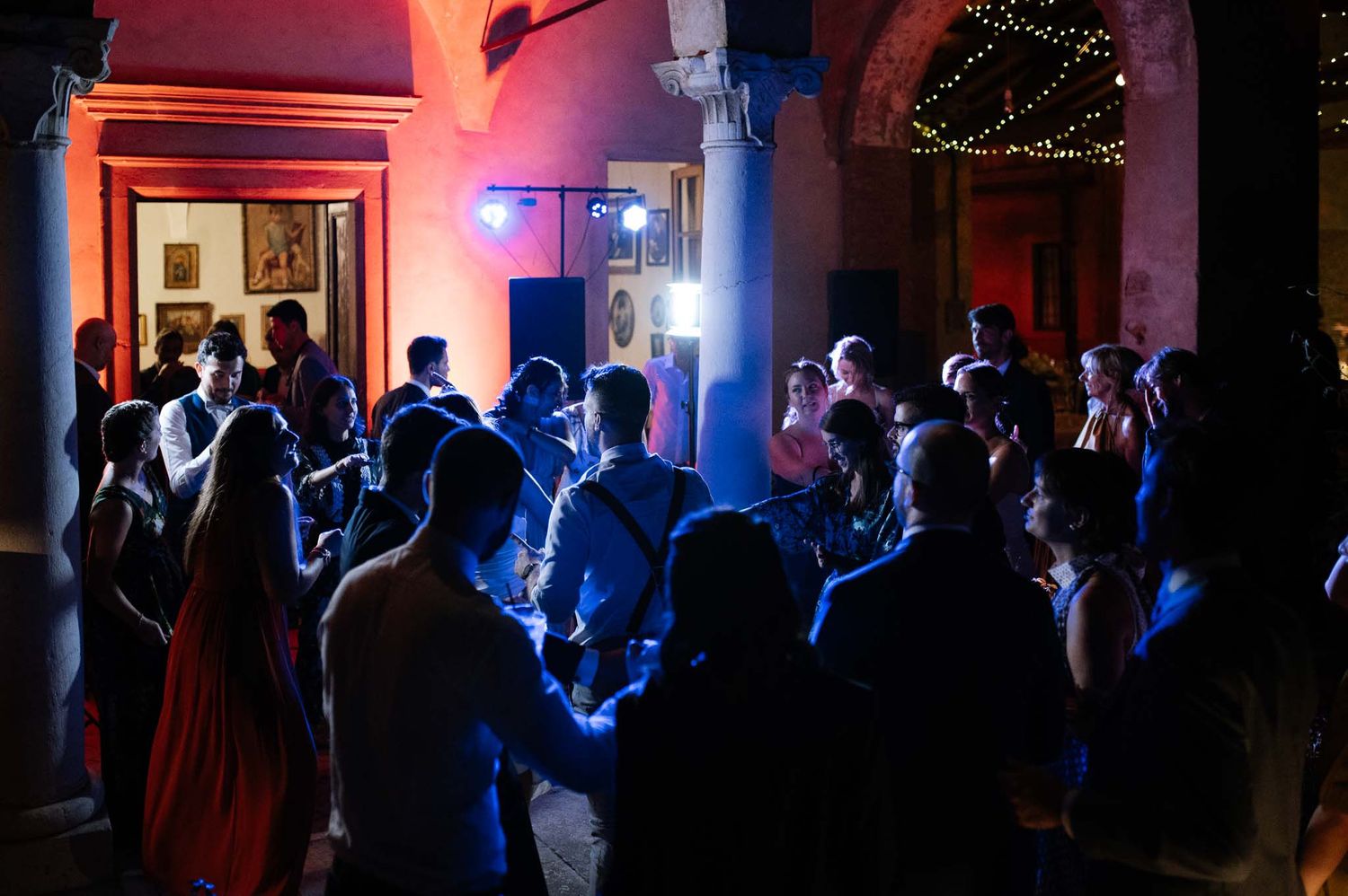 Silhouettes of party guests dancing in a dimly lit venue with blue and red lighting effects.