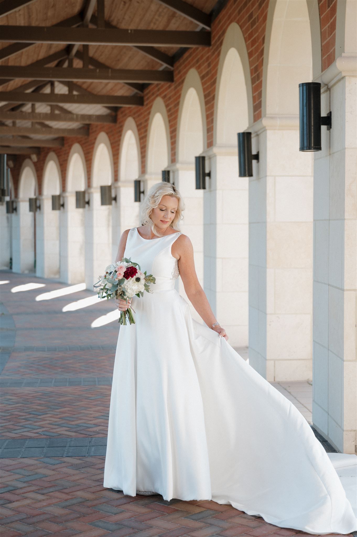 Bridal portrait in an elegant white gown under a covered walkway with arched columns.