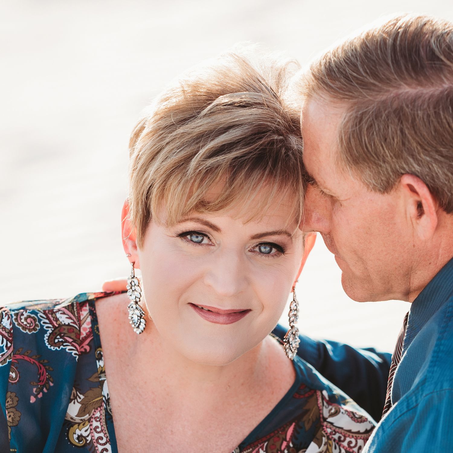 woman with blue eyes blonde hair sparkle earrings being hugged by man
