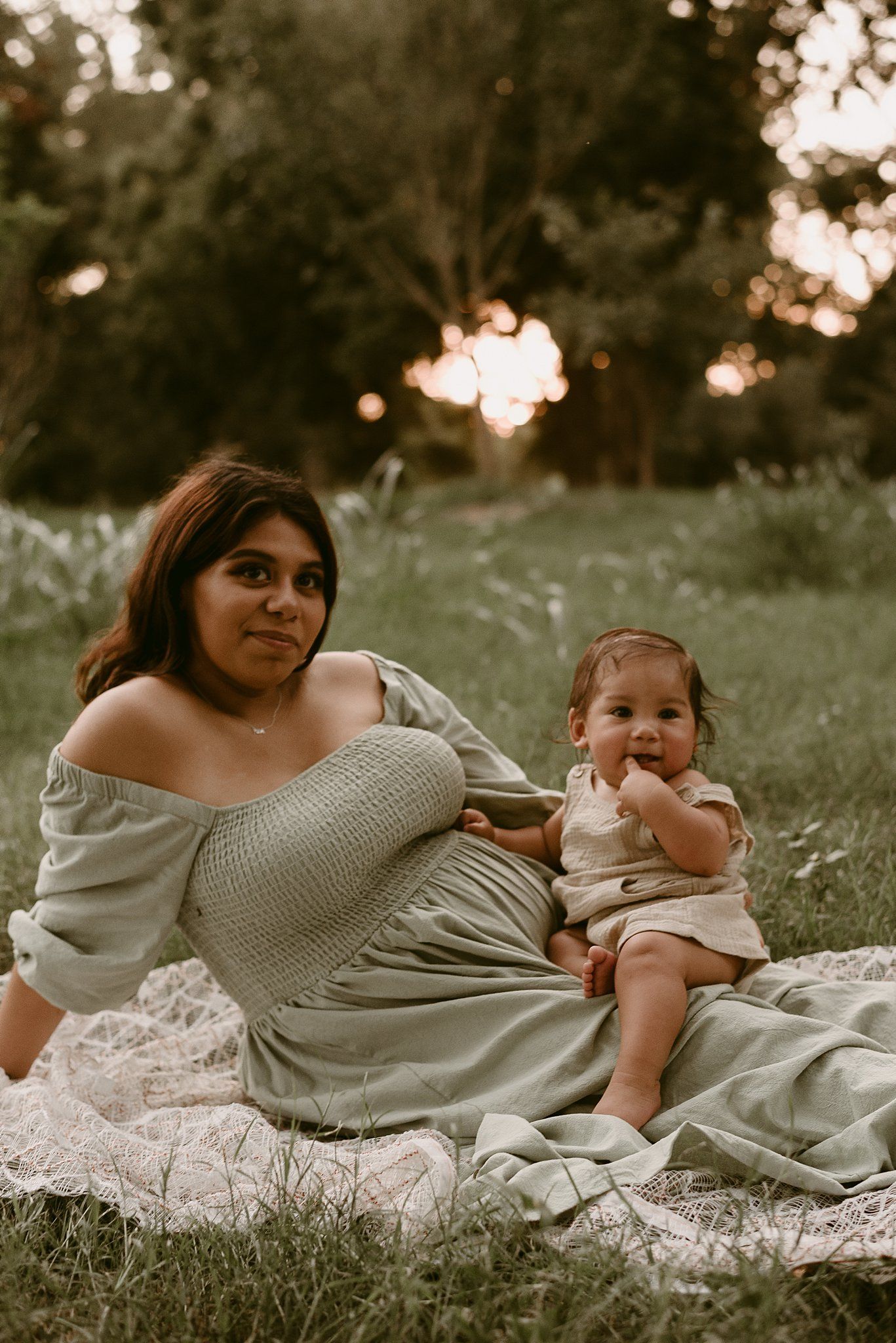 A heartwarming outdoor portrait of parent and baby sitting on lace during golden hour.