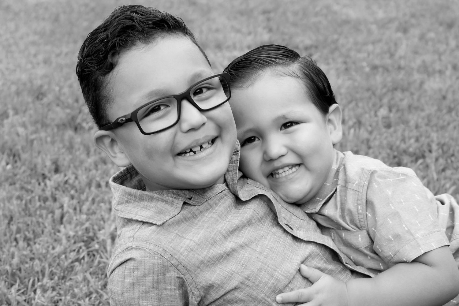 Black and white portrait of two smiling children sitting close together outdoors.