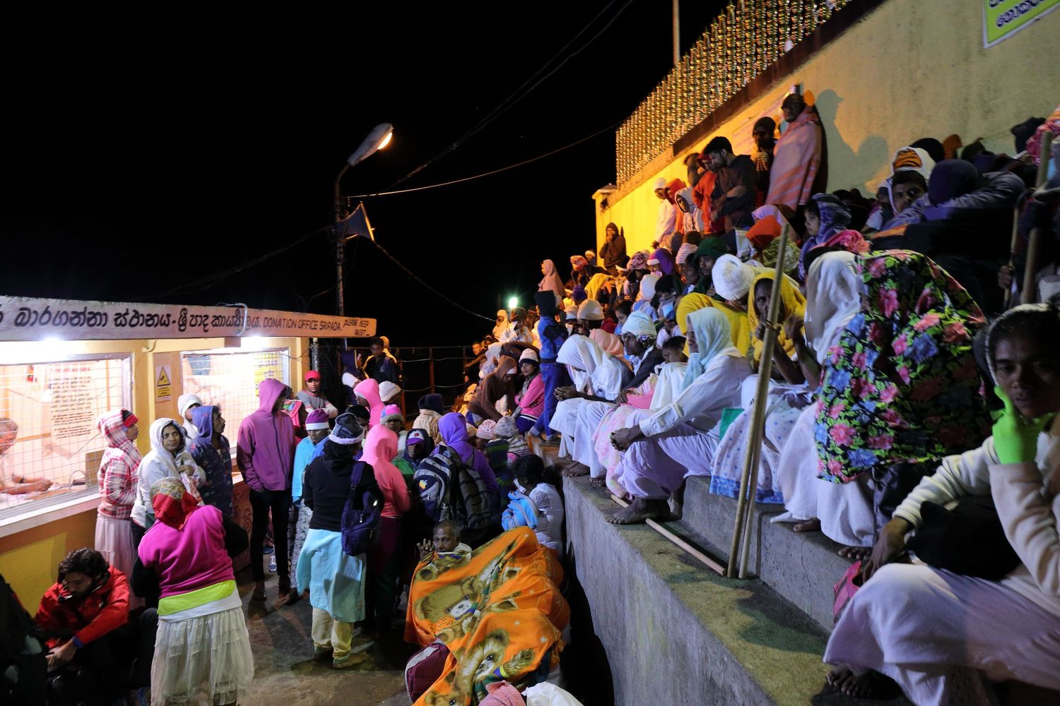 Nighttime festival gathering with illuminated crowd seated on tiered steps.