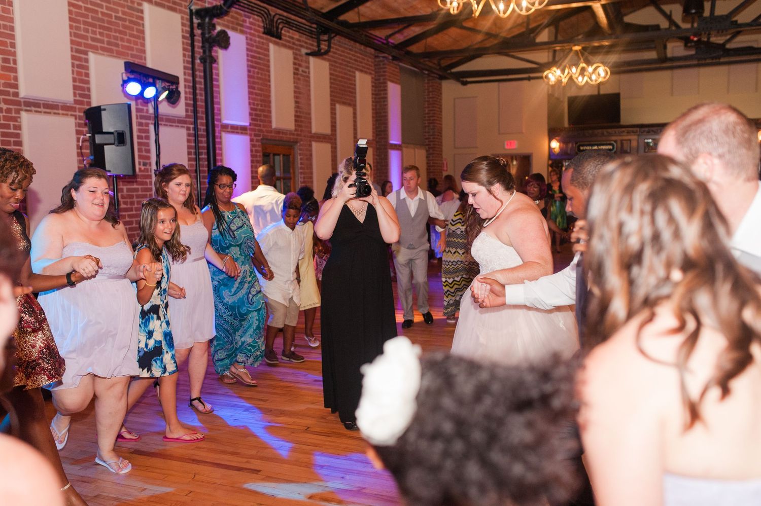 Wedding guests dancing together on a crowded dance floor at an indoor reception with warm lighting.