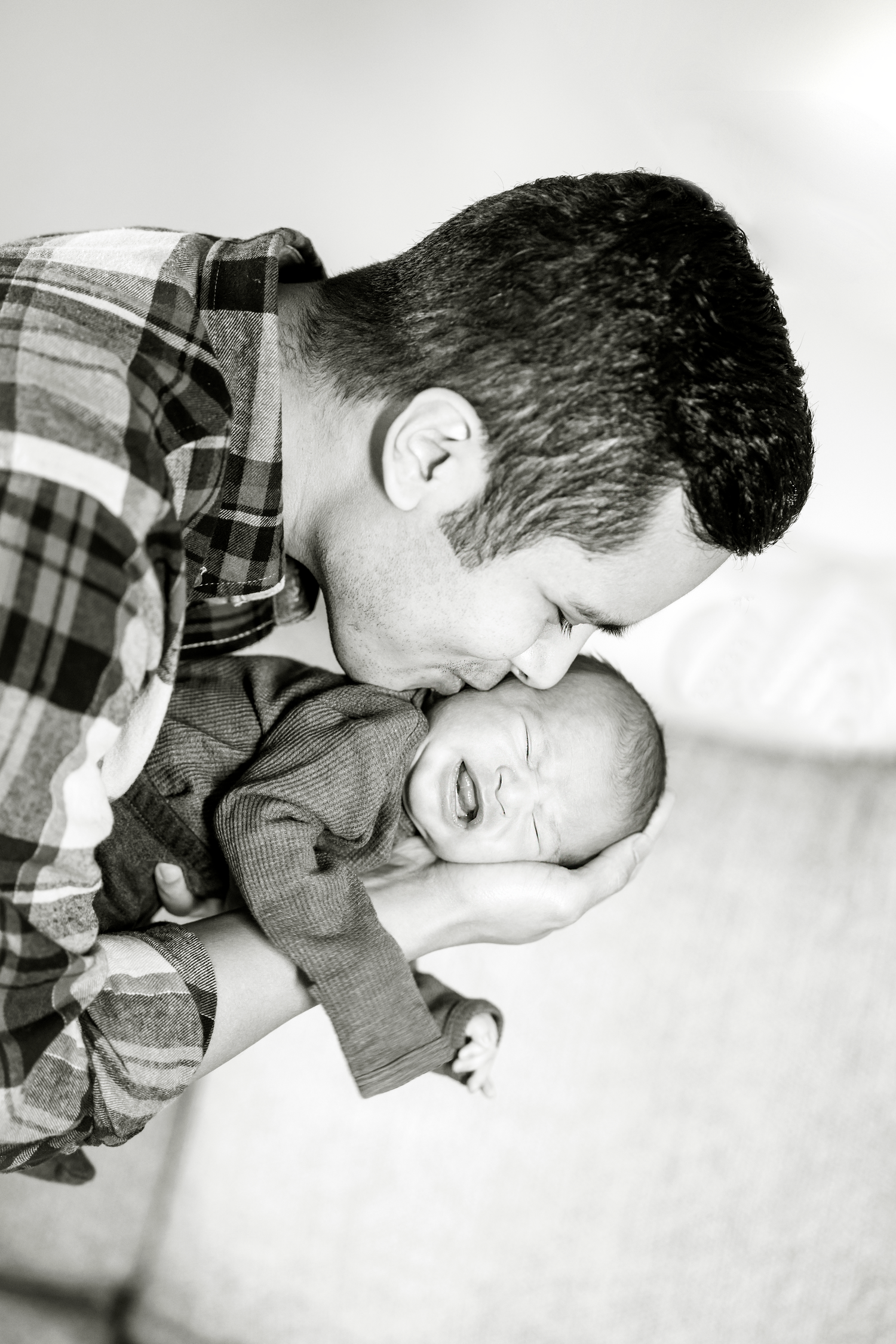 A black and white photo series showing a tender moment between parent and baby in plaid shirt.
