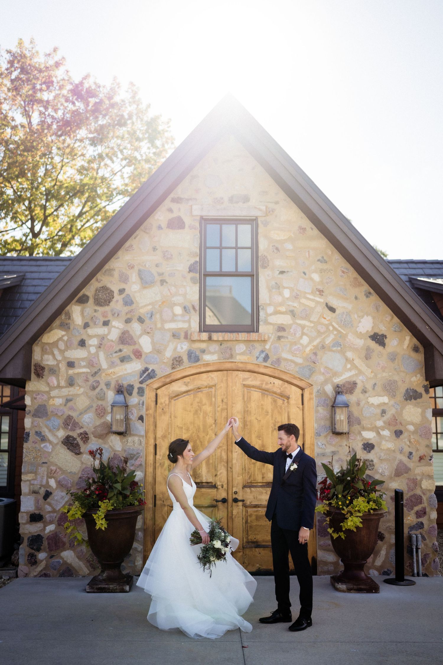 Elegant stone venue exterior with wooden arched door and potted plants creates romantic wedding backdrop.