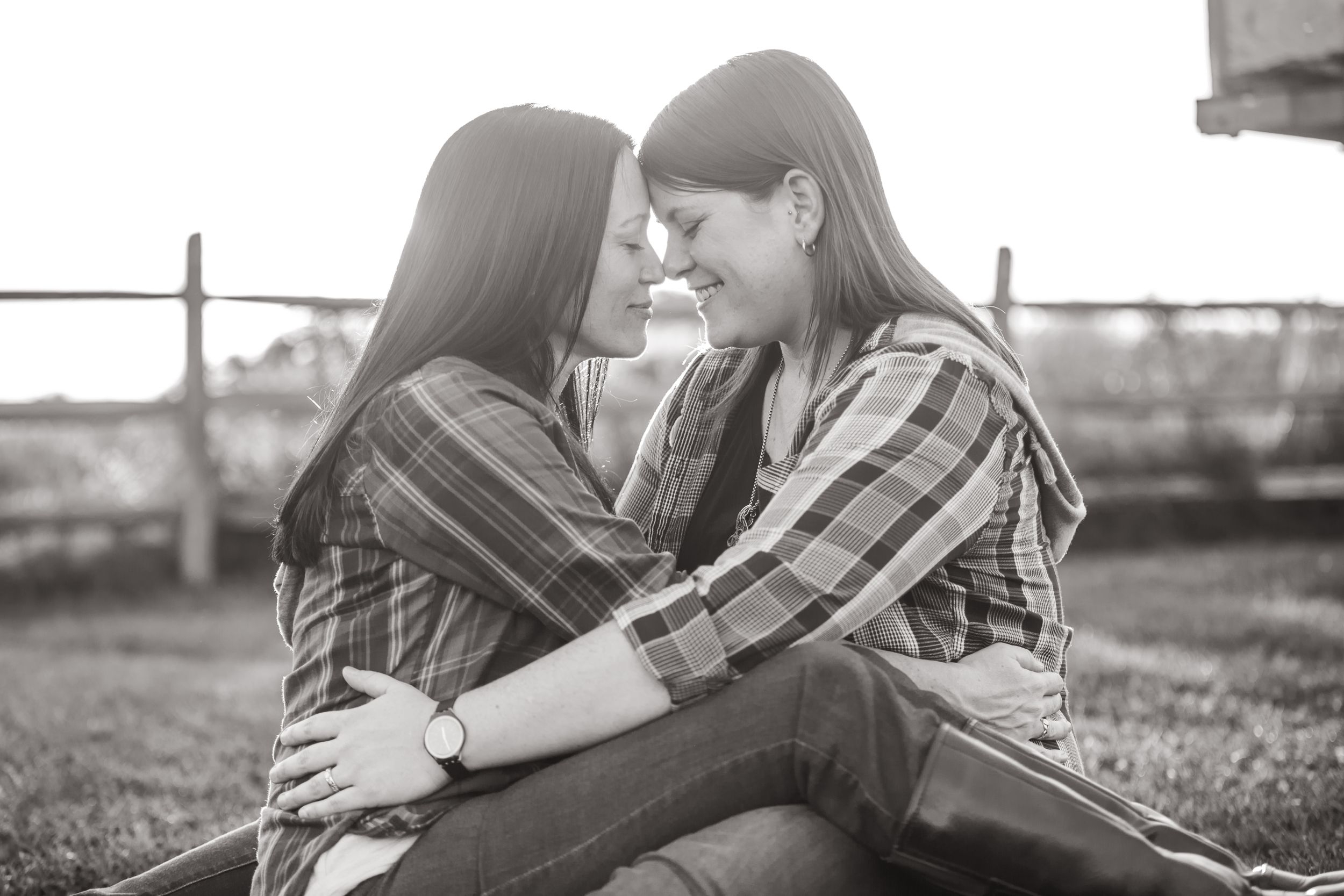 Two people share an intimate moment while sitting together outdoors in black and white.