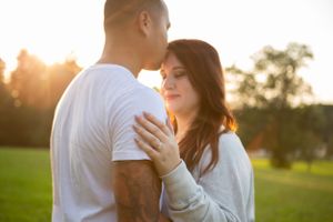 A tender embrace between a couple silhouetted against a sunset in a grassy field.