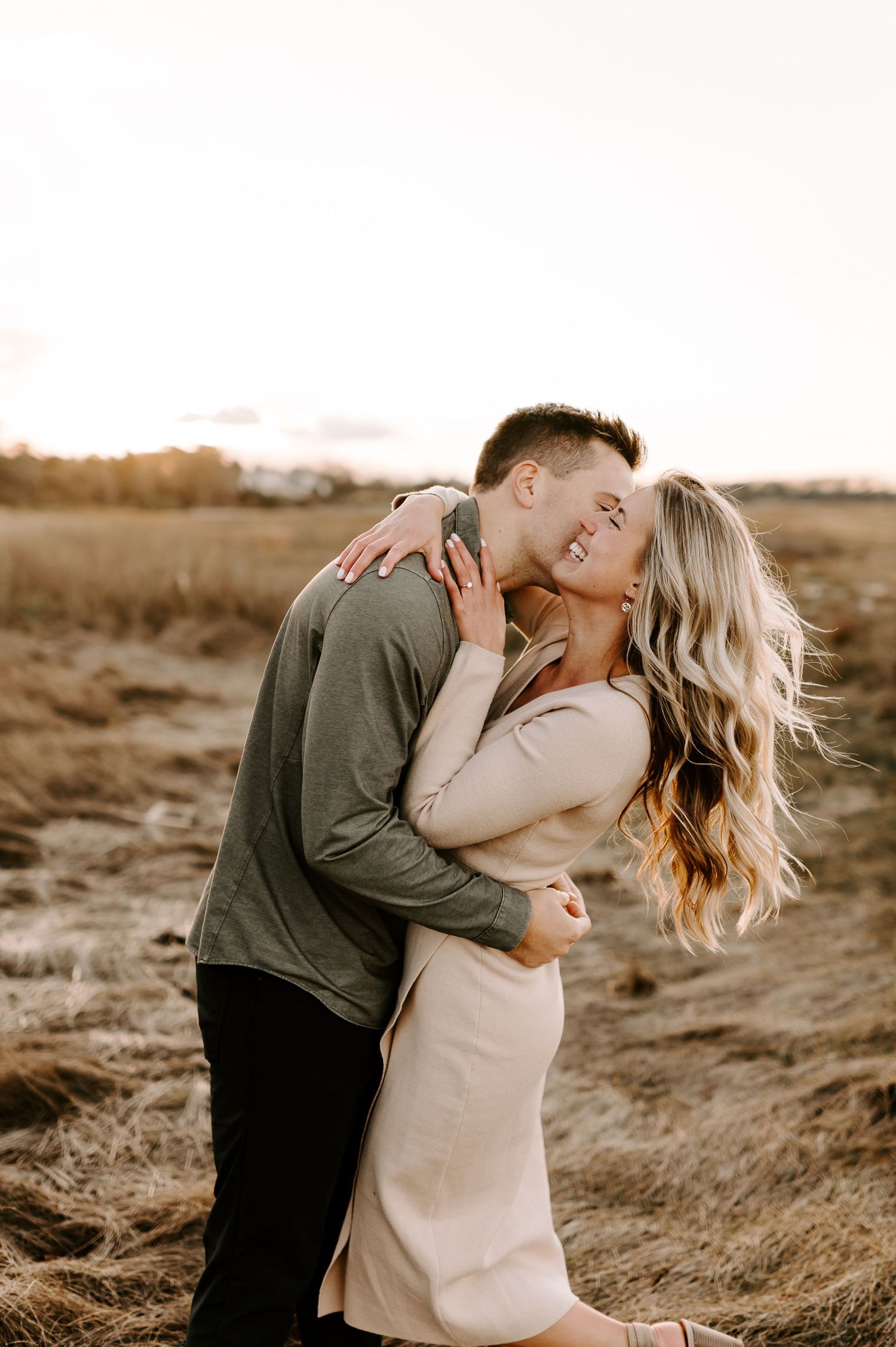 Couple shares tender kisses while standing in a rustic outdoor setting during golden hour.