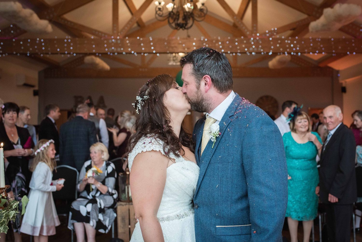 A romantic moment during a wedding reception in a rustic venue decorated with string lights.