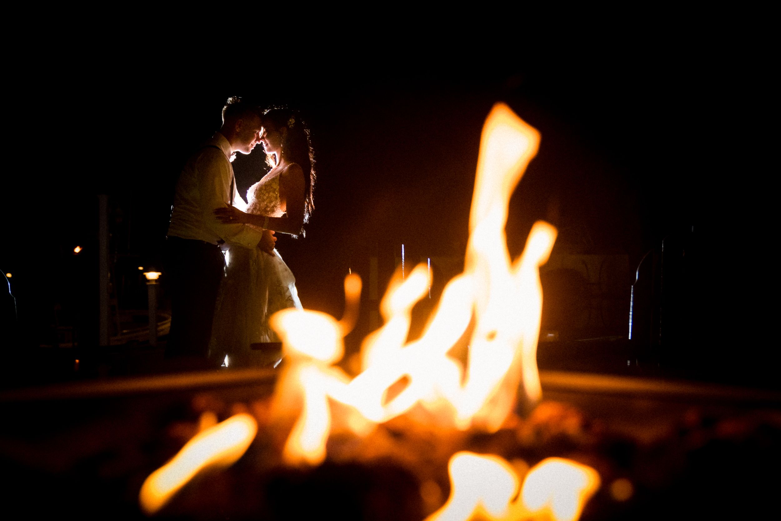 A cozy campfire blazes in the darkness with romantic silhouettes in the background.