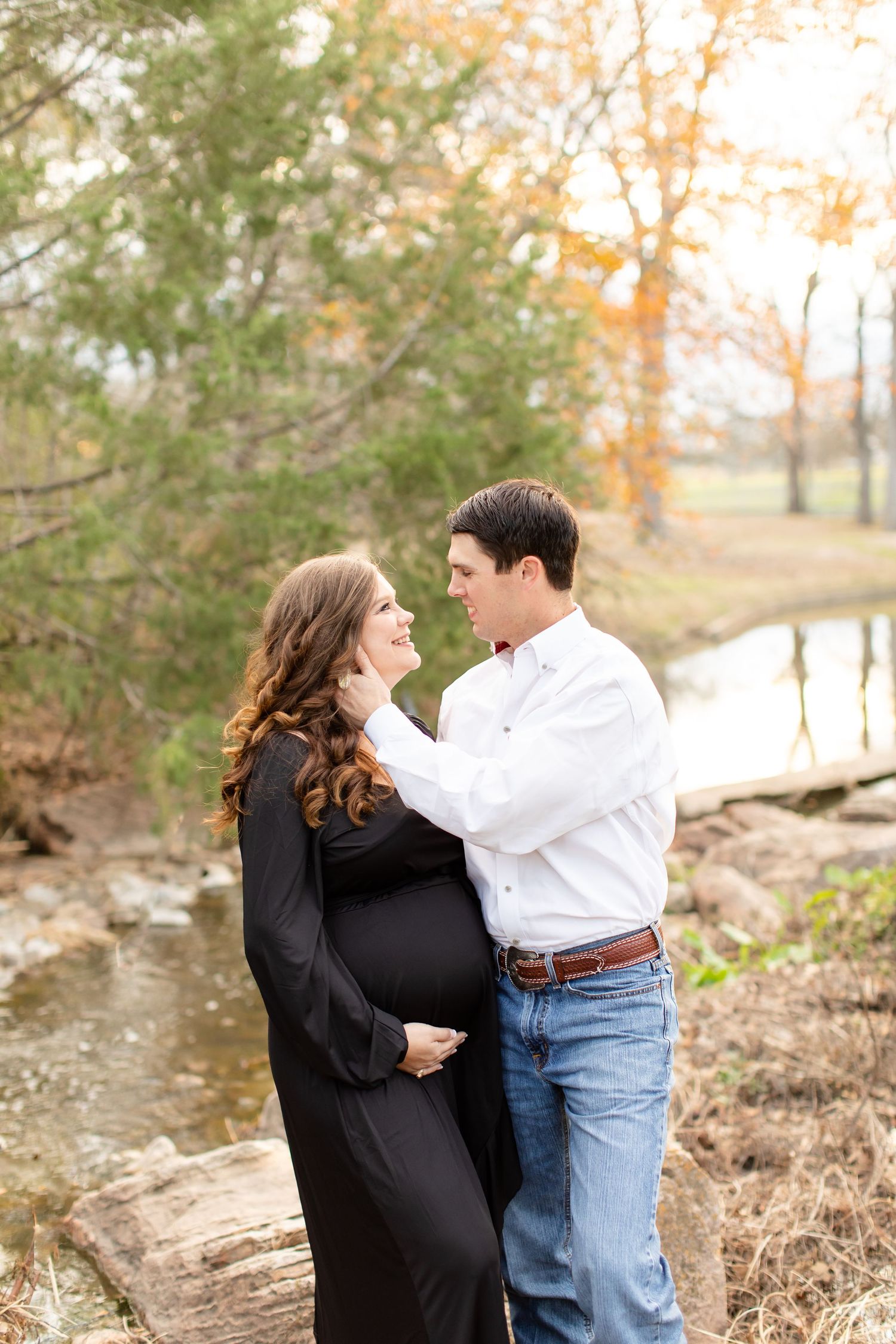 Tender moment between couple during creek-side maternity photoshoot.