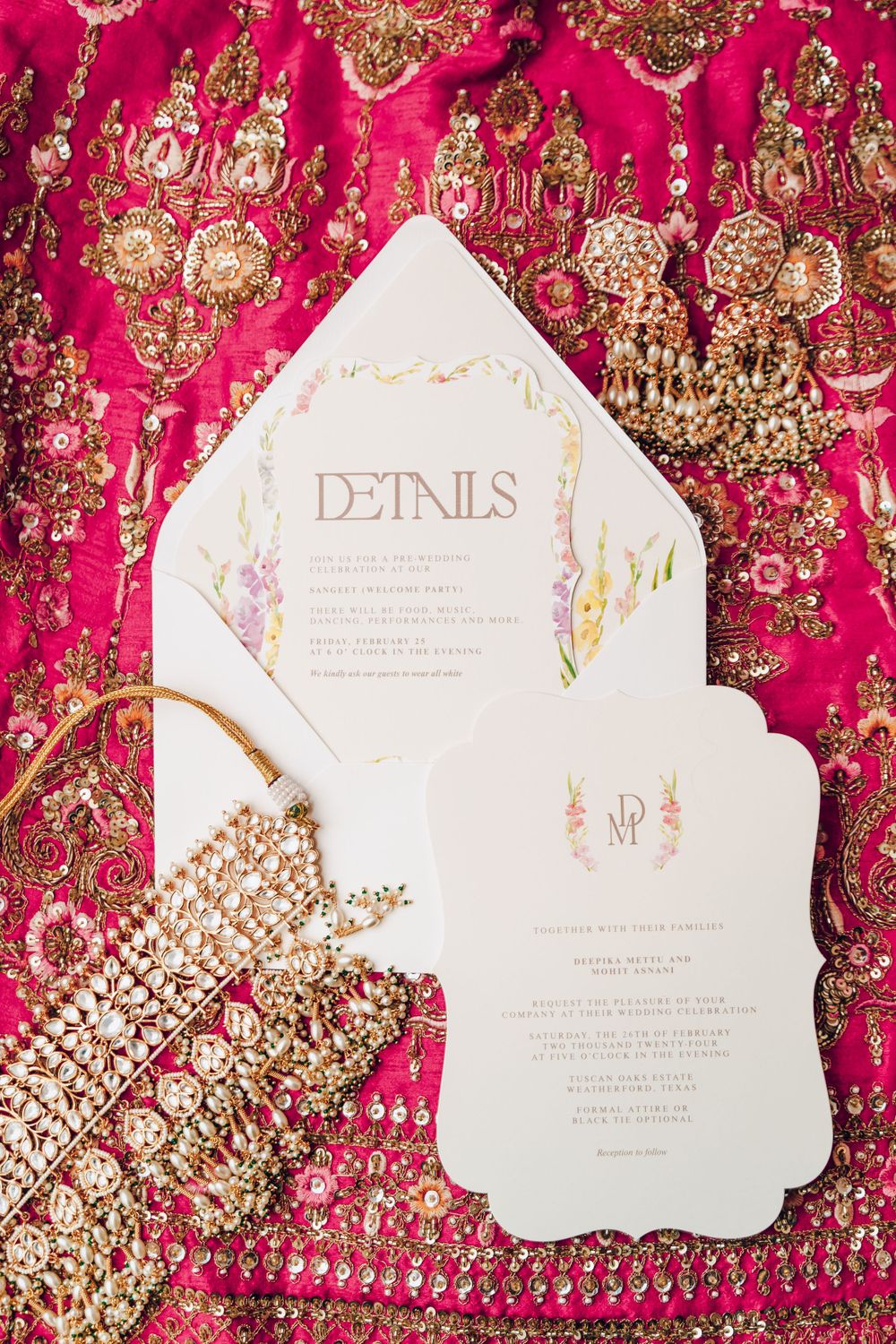 White wedding invitation details cards displayed on vibrant pink and gold embroidered fabric background.