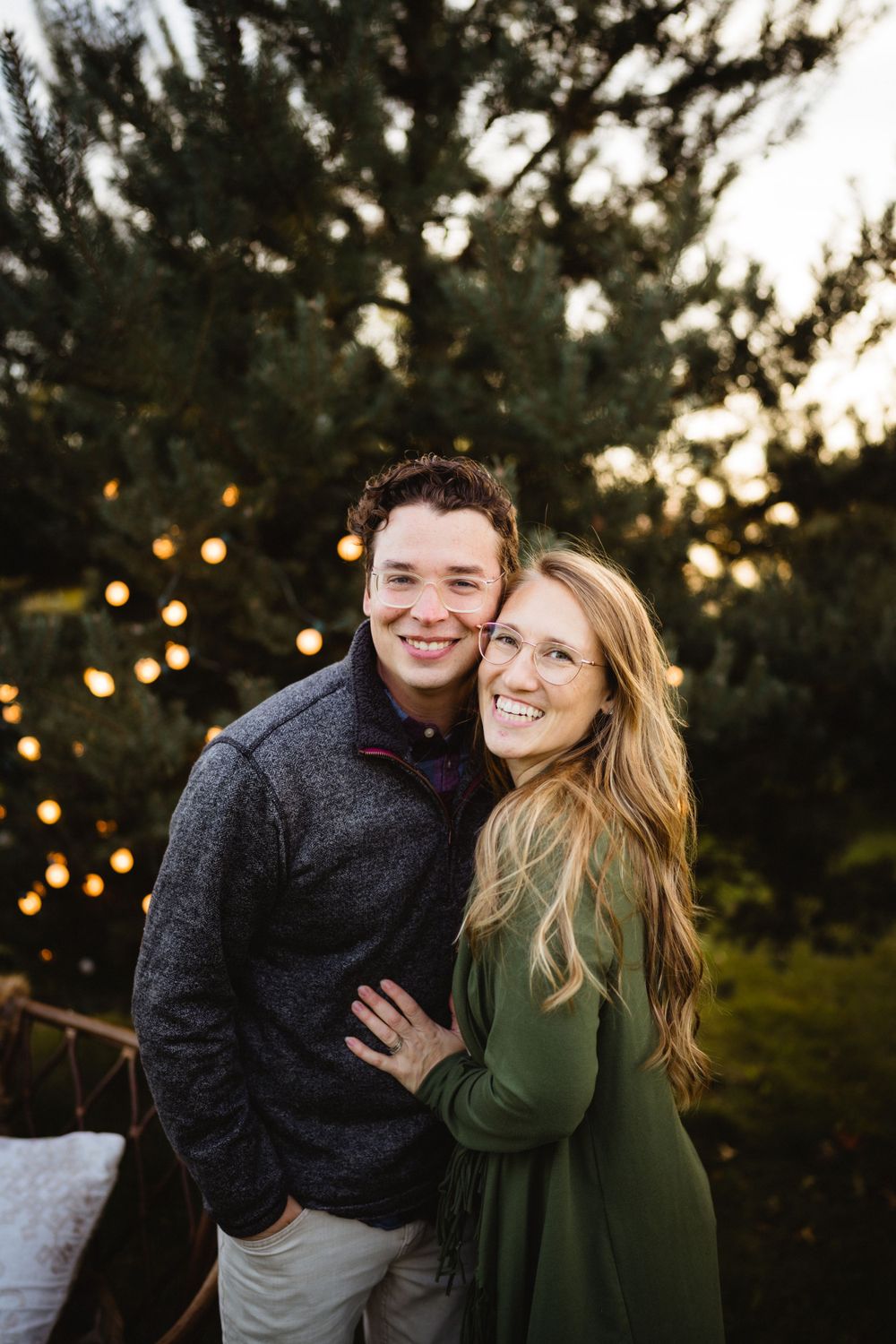 Couple sharing a joyful moment together against a backdrop of evergreen trees and twinkle lights.